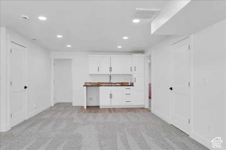 Spacious open room featuring a built-in wet bar with white cabinetry and a stainless steel sink