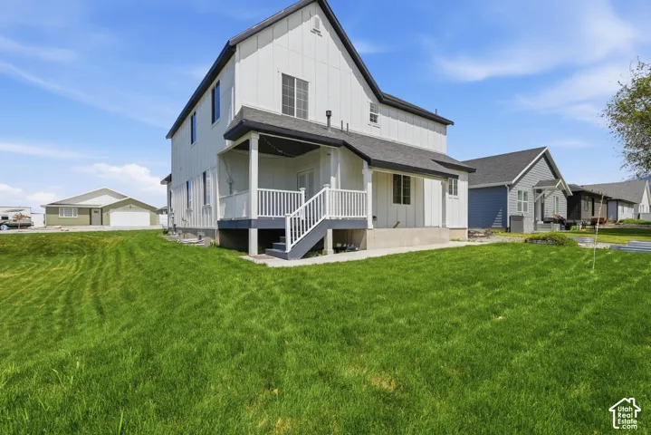 Expansive green lawn surrounding a modern two-story residence featuring white vertical siding, a dark gray shingle roof, and a covered back porch with white railings and steps