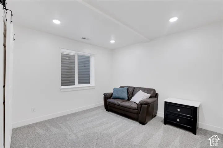 Carpeted room featuring a white-framed window, recessed lighting, and a white barn door on a black rail system