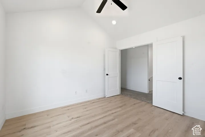 Interior room featuring wood-finish flooring, white baseboards, and a vaulted ceiling with a black ceiling fan