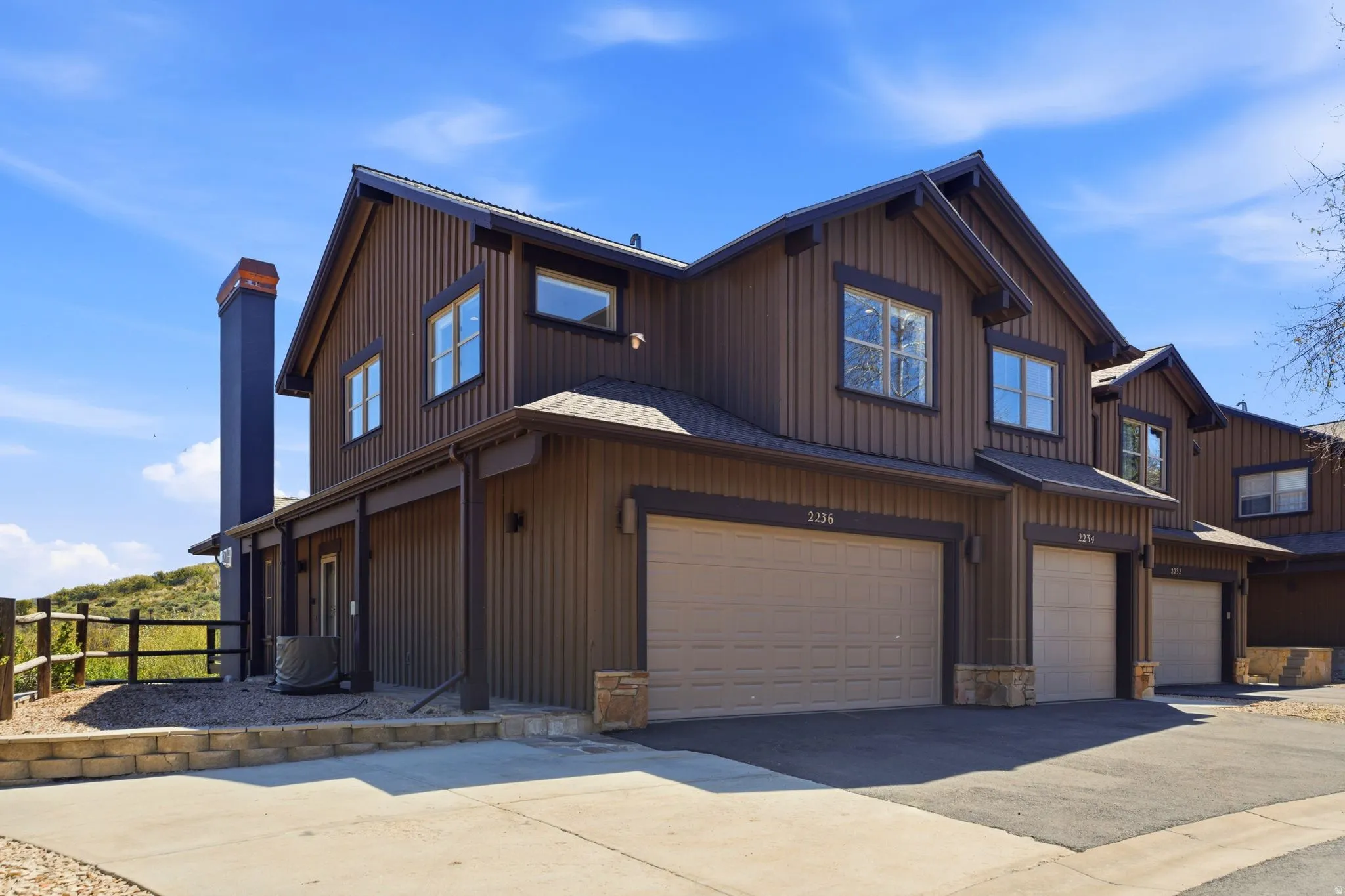 Brown vertical board siding exterior with multiple pitched gables, attached garage, stone accents, and dark trim