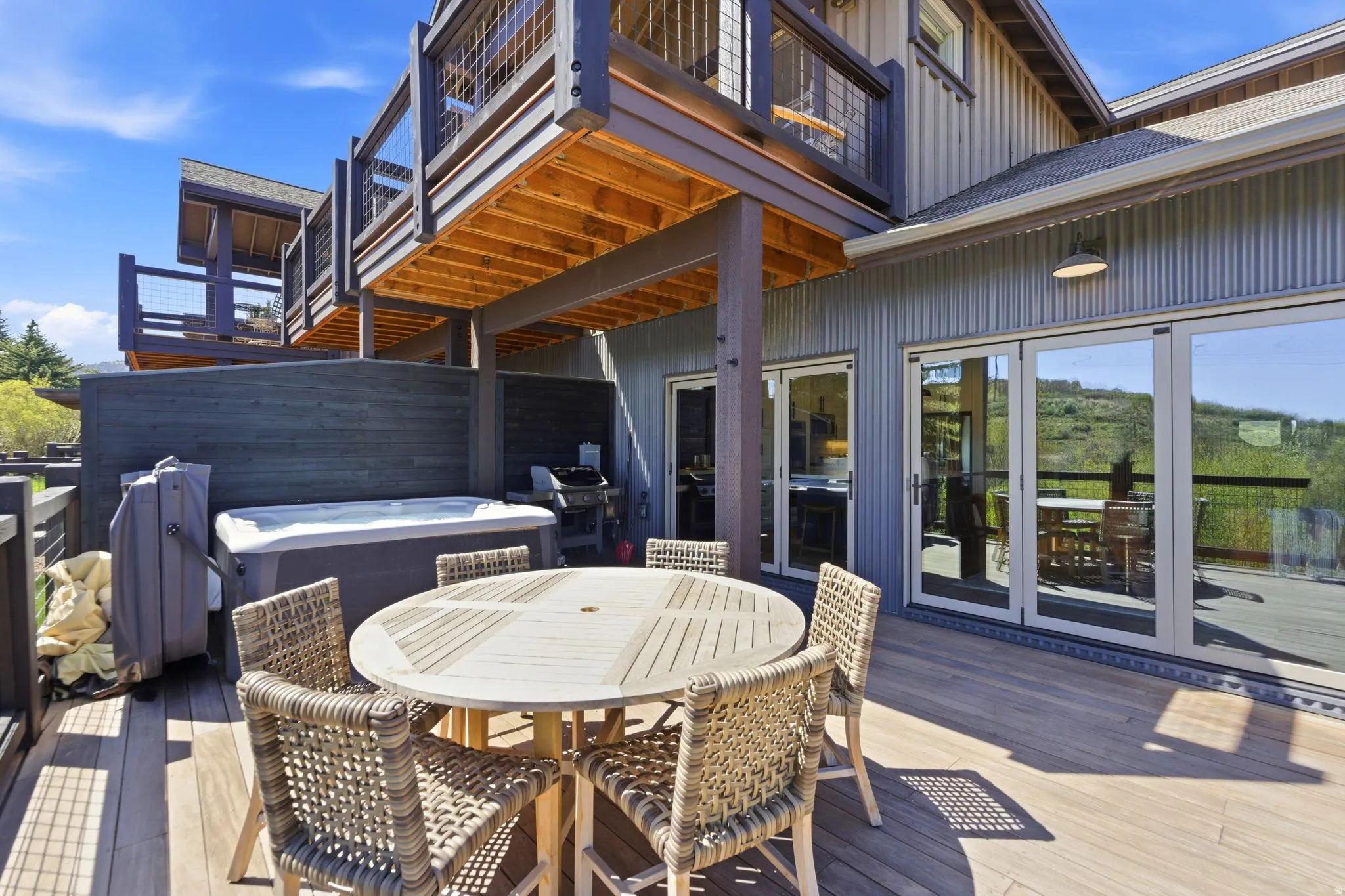 Spacious outdoor deck featuring wide plank wood-finish flooring, a built-in spa, a large round outdoor table, and multiple sets of glass panel doors