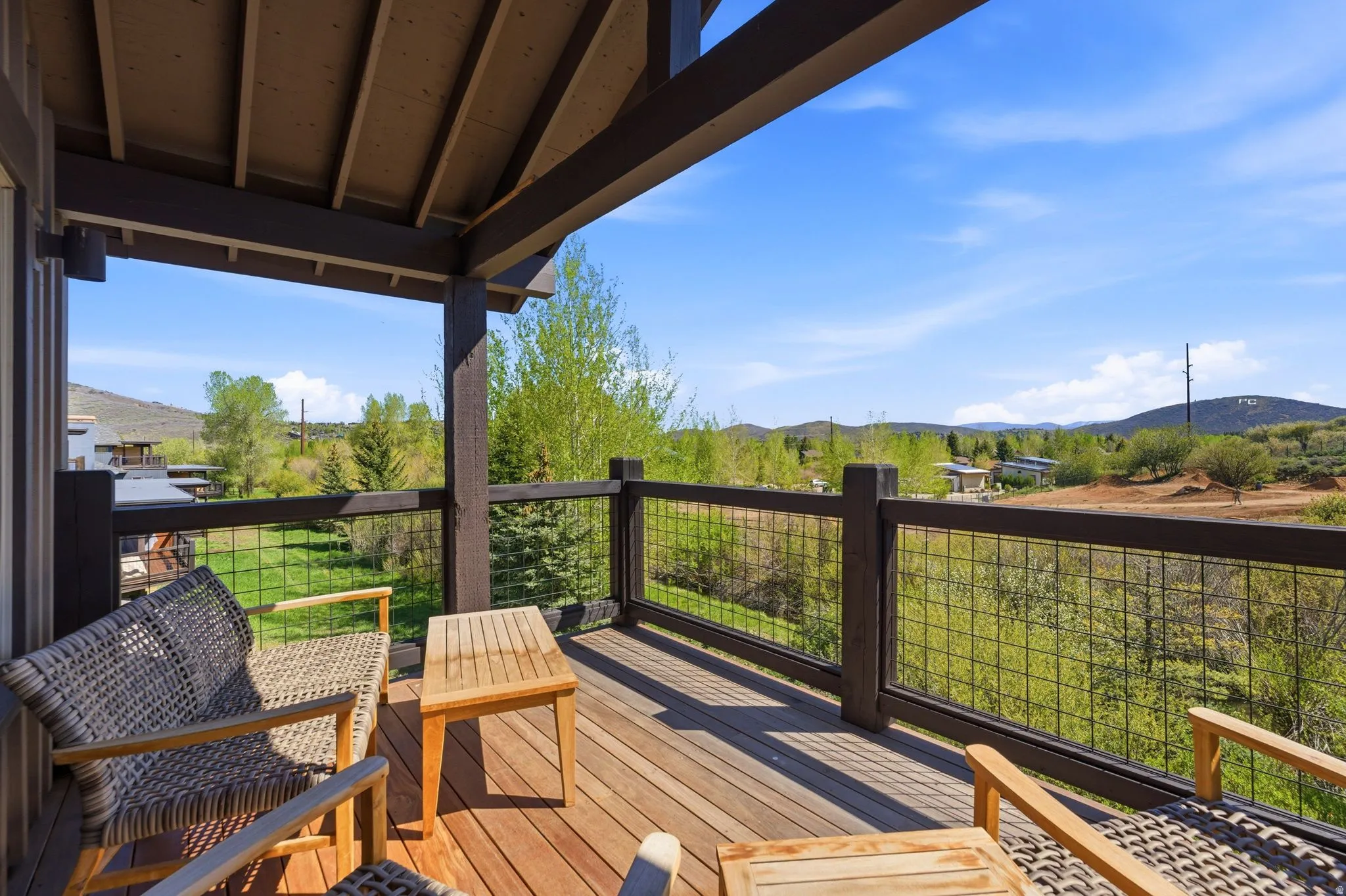 Covered outdoor deck with wood-finish flooring, dark wood railings, and mesh infill