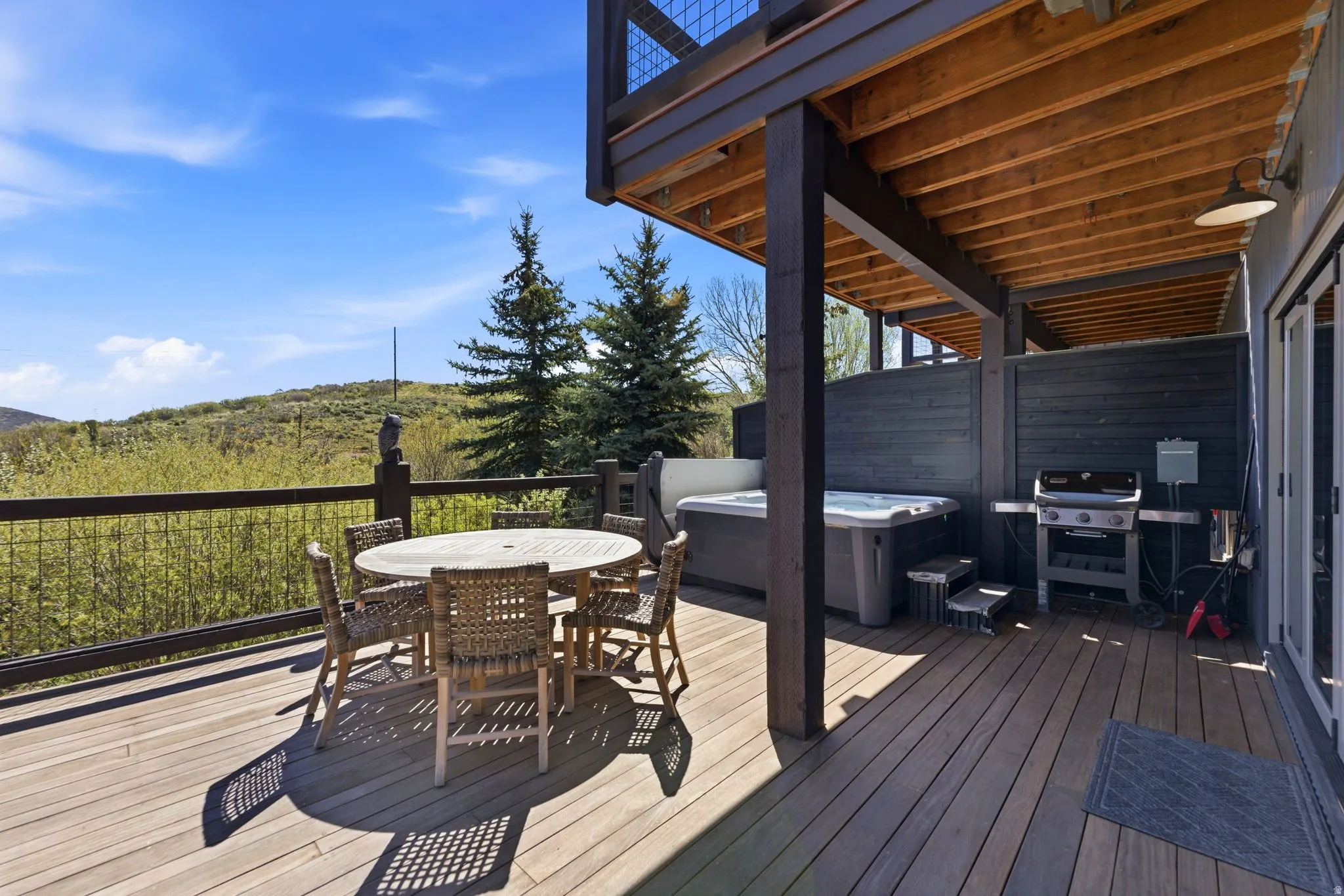 Expansive wood deck featuring a hot tub, built-in grill, wire railing, and a slatted privacy wall
