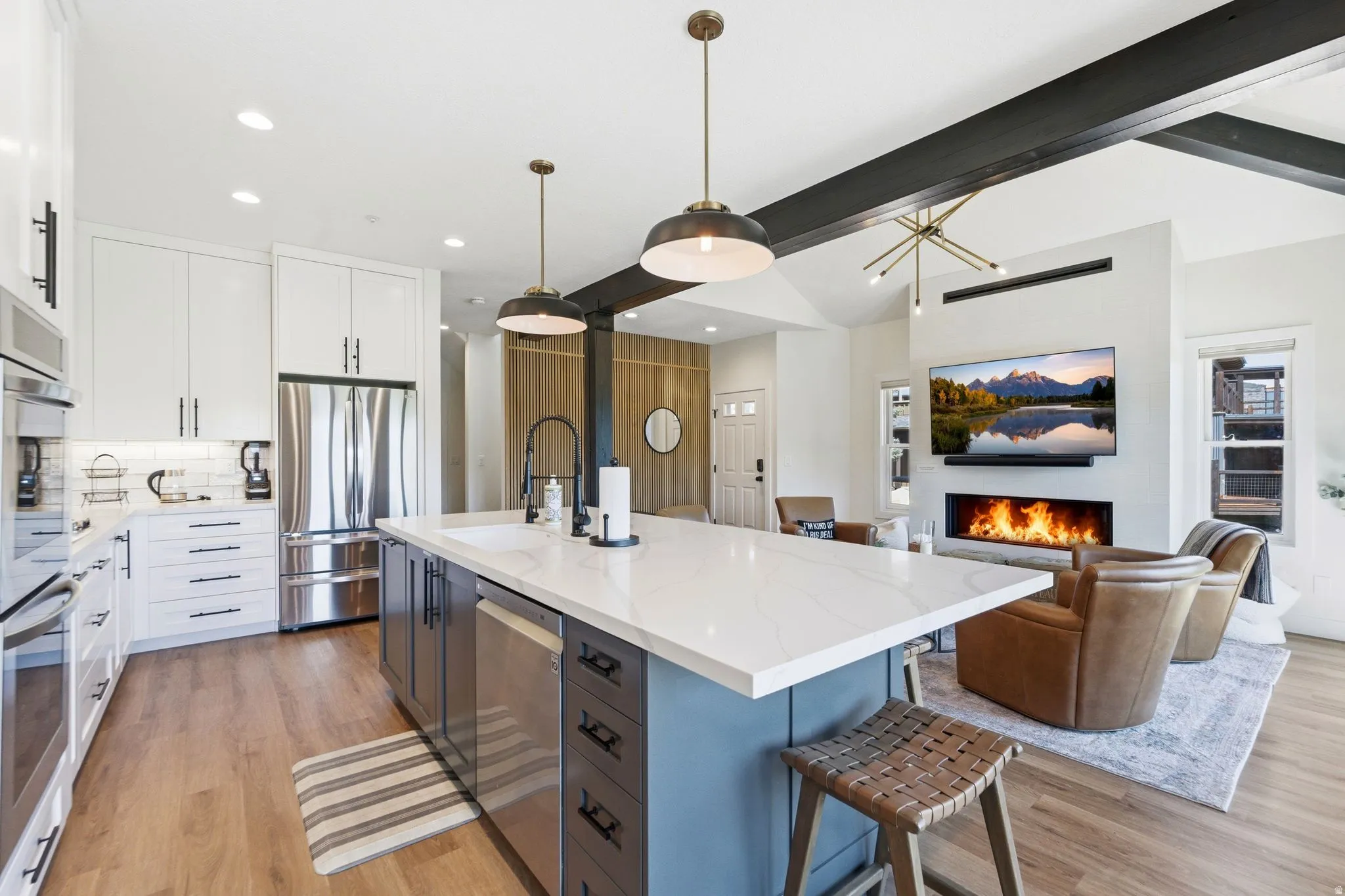 Open-concept kitchen and living area featuring a large center island with a white countertop and seating, stainless steel appliances, and wood-finish flooring