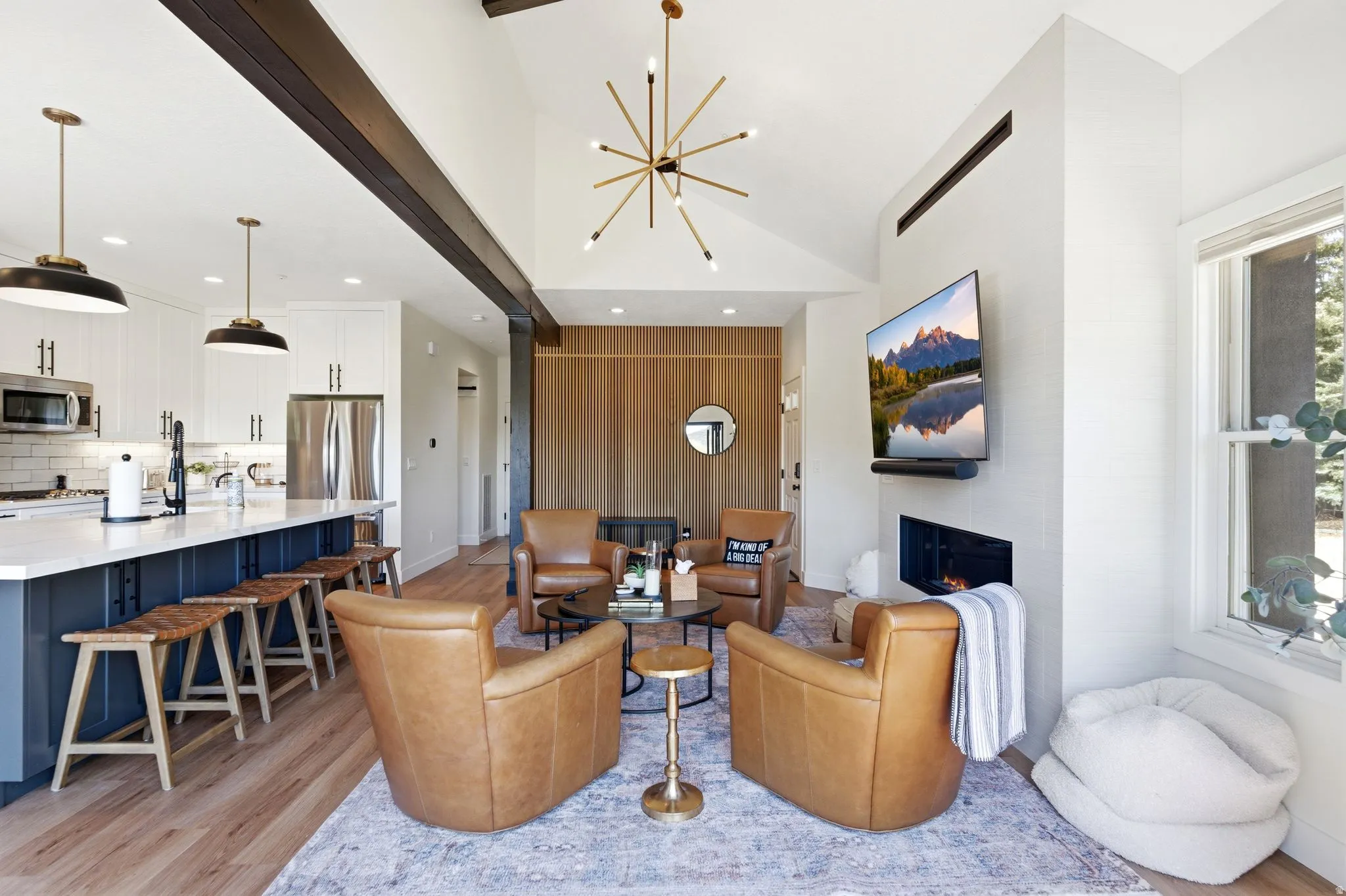 Open concept living area featuring vaulted ceilings with exposed beams, a contemporary fireplace, and wood-finish flooring
