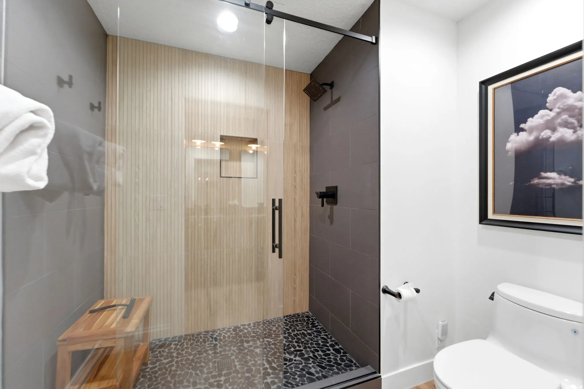 Glass-enclosed shower featuring a dark pebble-finish floor, wood-finish wall paneling, and matte black fixtures