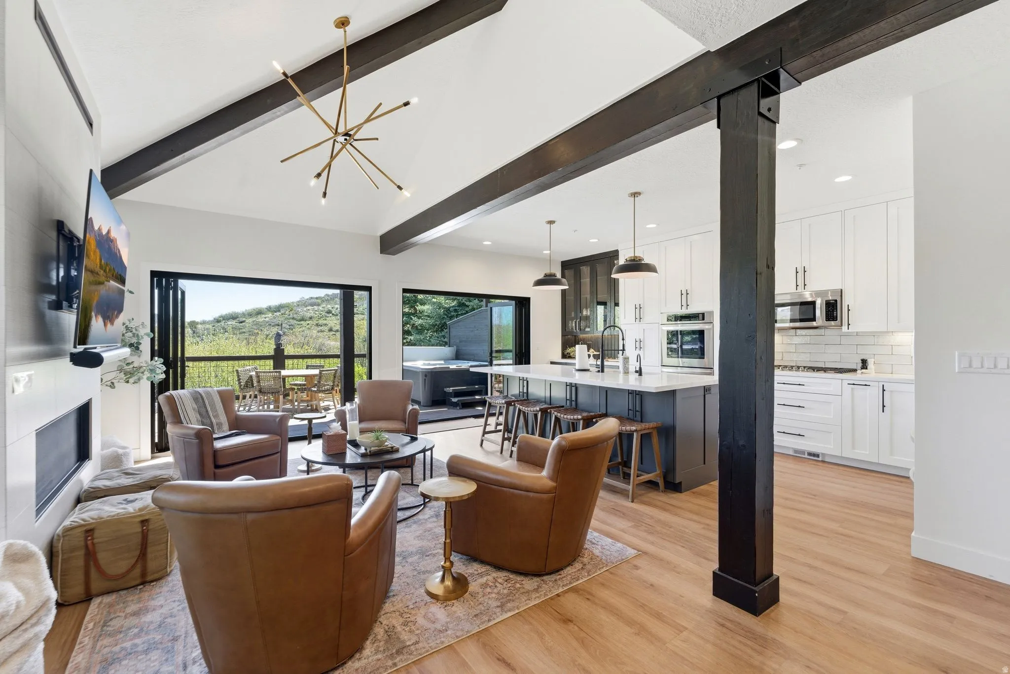 Open-concept living space featuring vaulted ceilings with exposed wood beams, wood-finish flooring, a contemporary fireplace, and a gourmet kitchen with a central island and stainless steel appliances