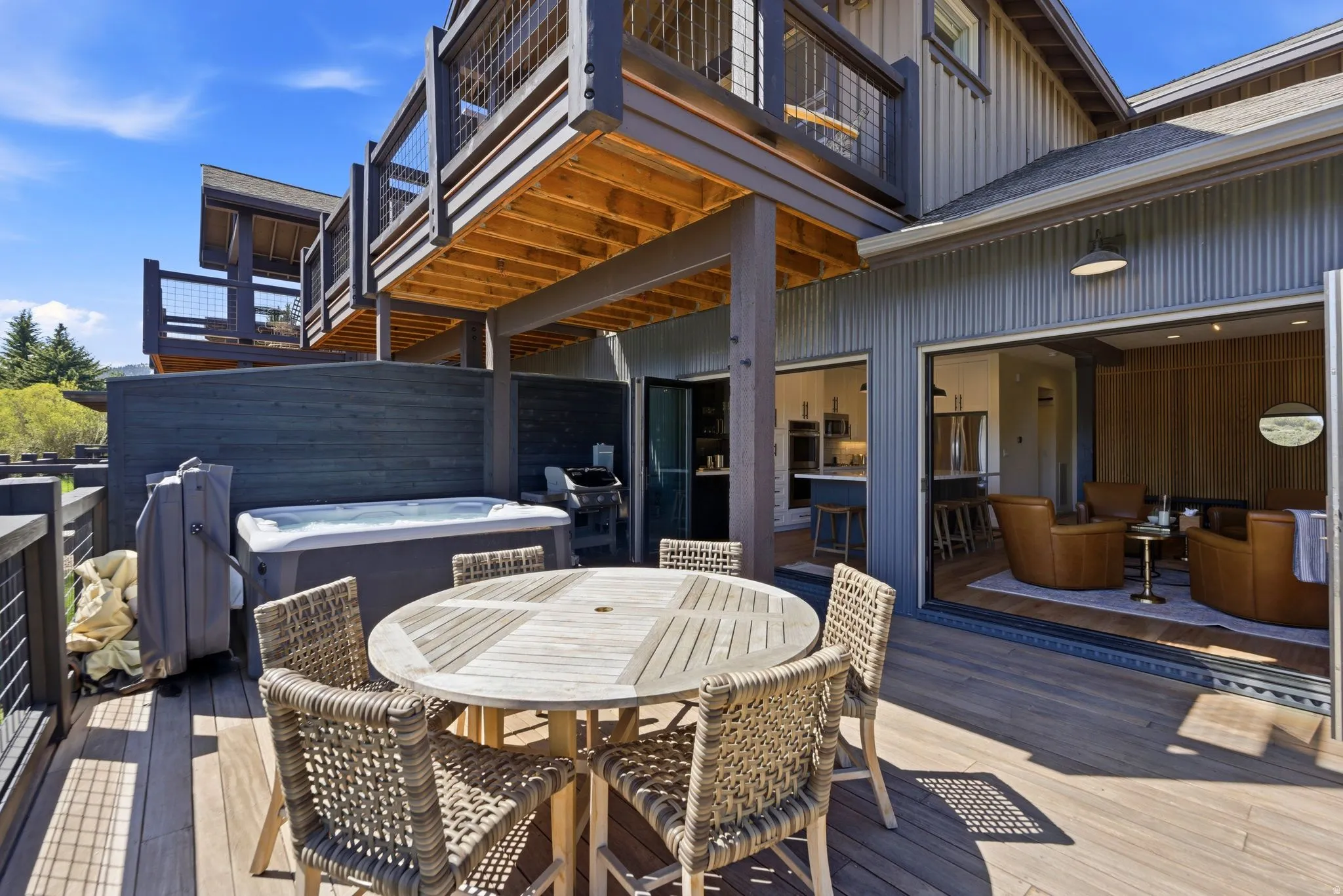Expansive exterior decking featuring a hot tub, an outdoor dining area, and multiple balconies with metal railings