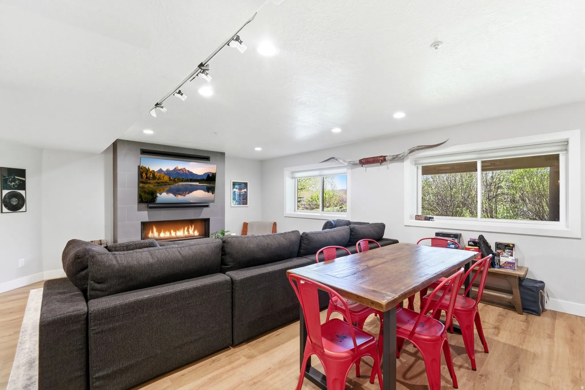 Open-concept living space featuring wood-finish flooring, a contemporary fireplace with a stone surround, and recessed lighting