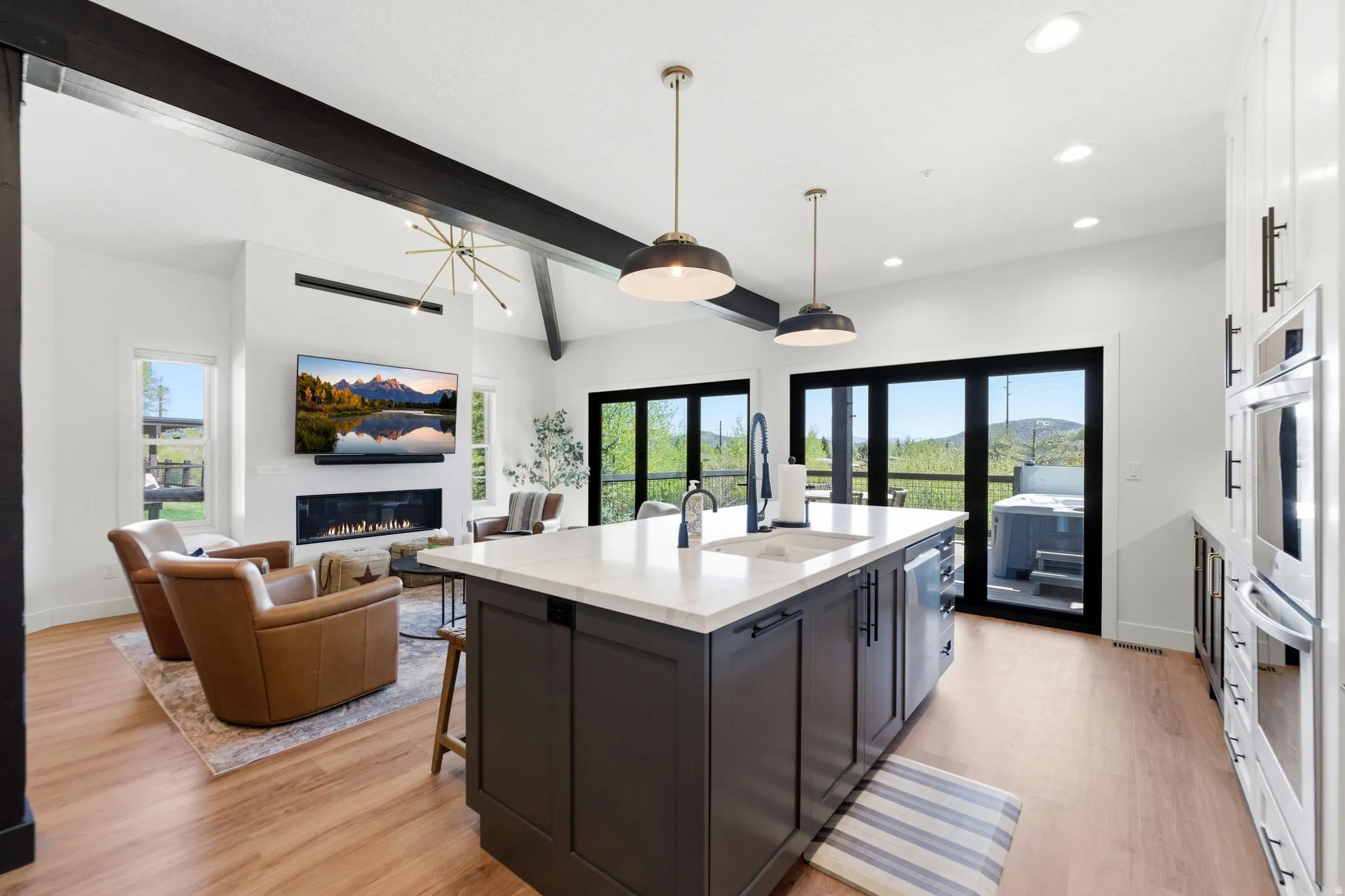Open-concept living space featuring a central kitchen island with a white countertop and dark cabinetry, wood-finish flooring, and a linear fireplace