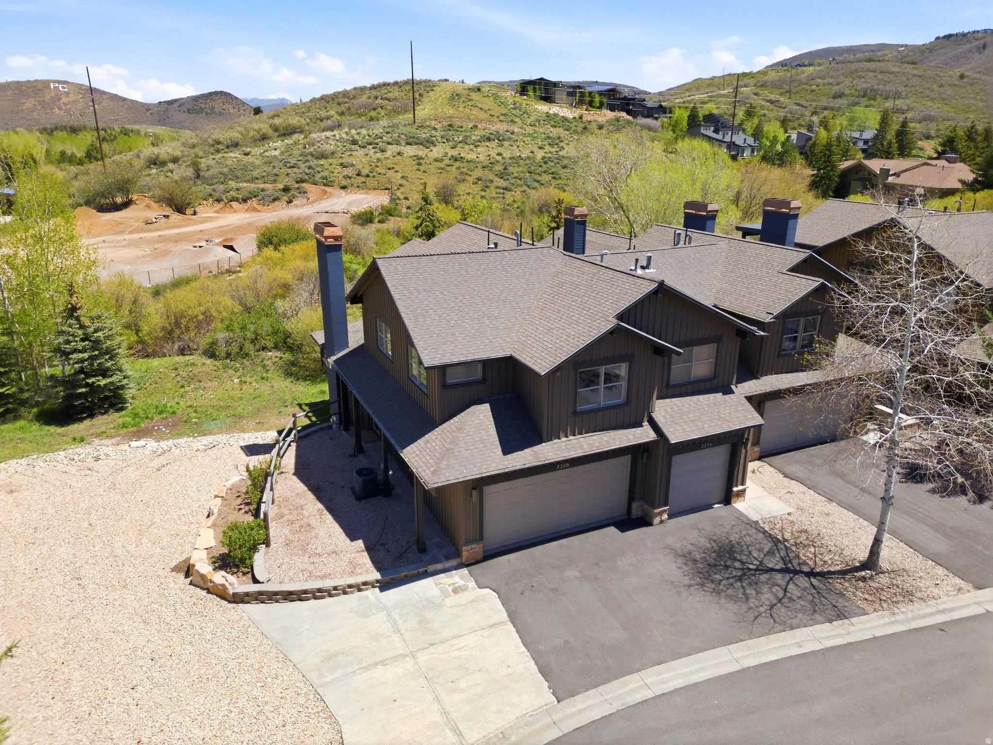 Multi-level residence featuring a brown siding exterior, a dark shingle roof, and multiple chimneys with stone accents