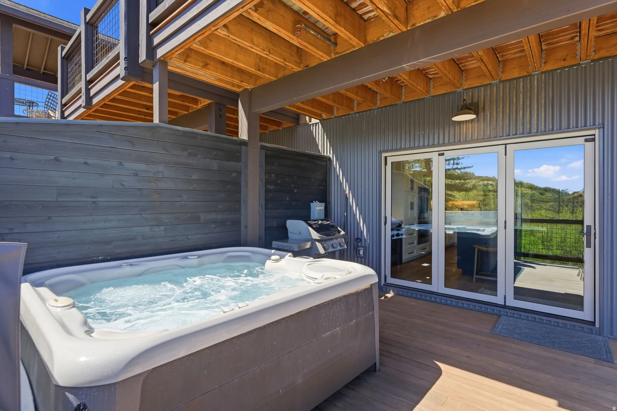 Outdoor hot tub with privacy wall, wood-finish decking, and bi-fold glass doors