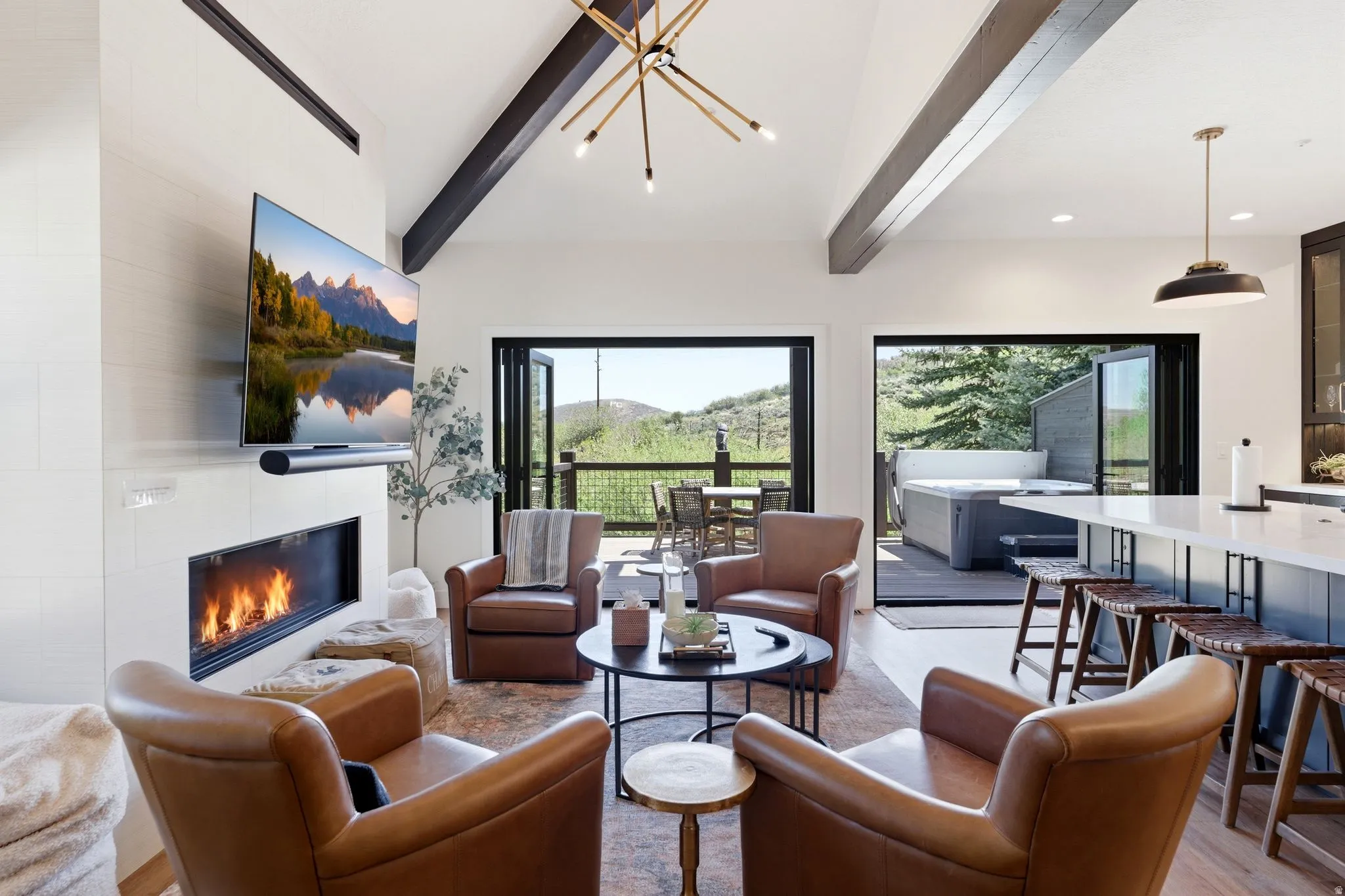 Open-concept living area with a contemporary fireplace, vaulted ceiling featuring exposed beams, and accordion-style glass doors