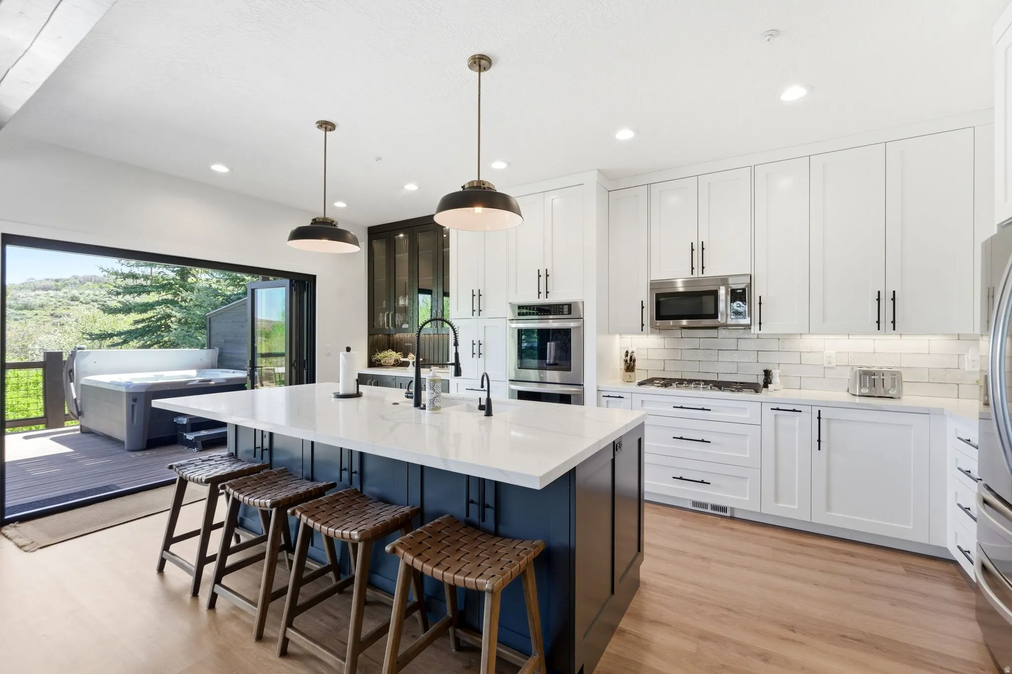 Gourmet kitchen featuring a large island with white countertop, integrated stainless steel appliances, white subway tile backsplash, and wood-finish flooring