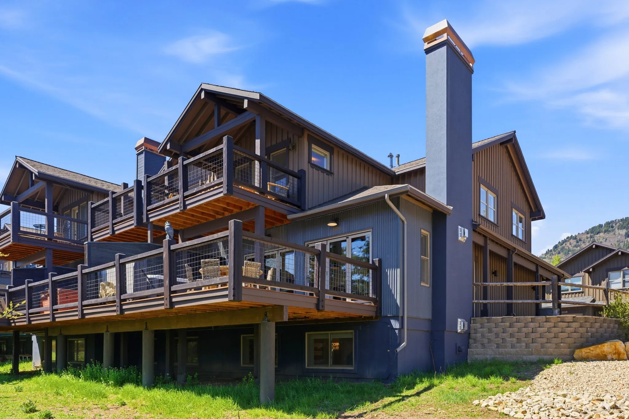 Multi-level decking with wire railing, a tall exterior chimney, and a stone retaining wall
