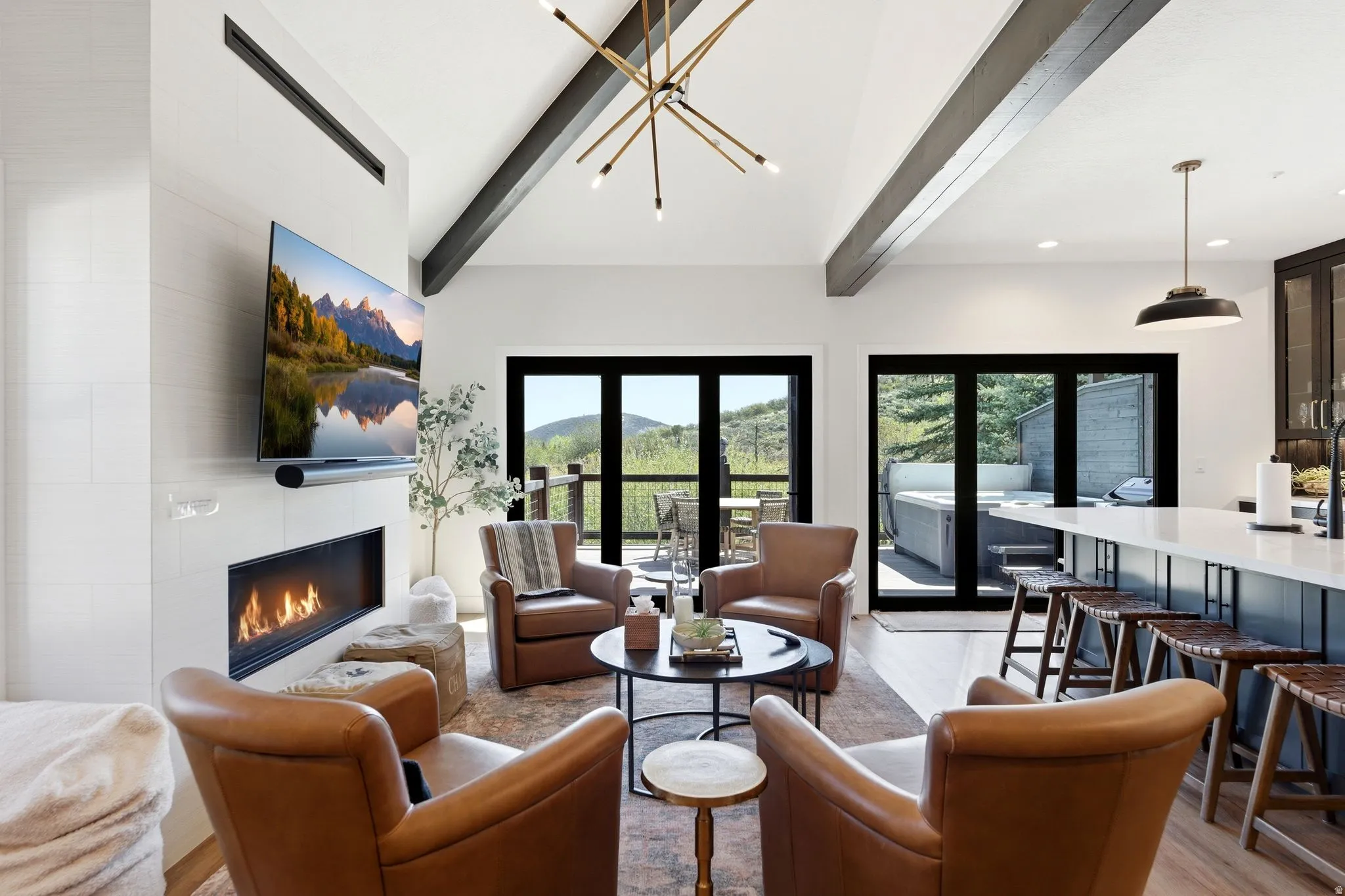 Open-concept living area featuring vaulted ceilings with exposed beams, a linear fireplace, and multiple sets of black-framed glass doors