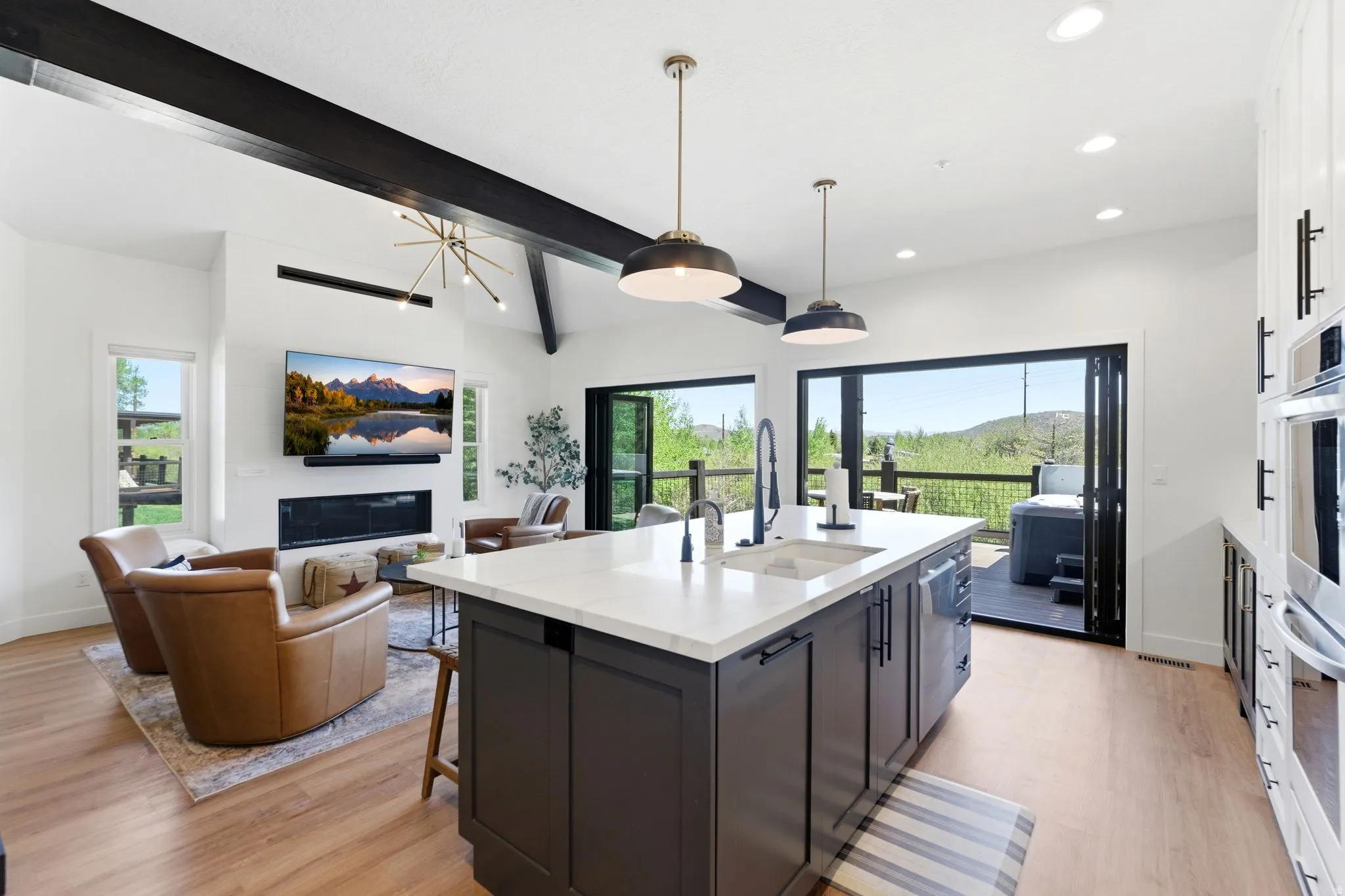 Open-concept kitchen and living area featuring wood-finish flooring, a kitchen island with sink, integrated dishwasher, and pendant lighting