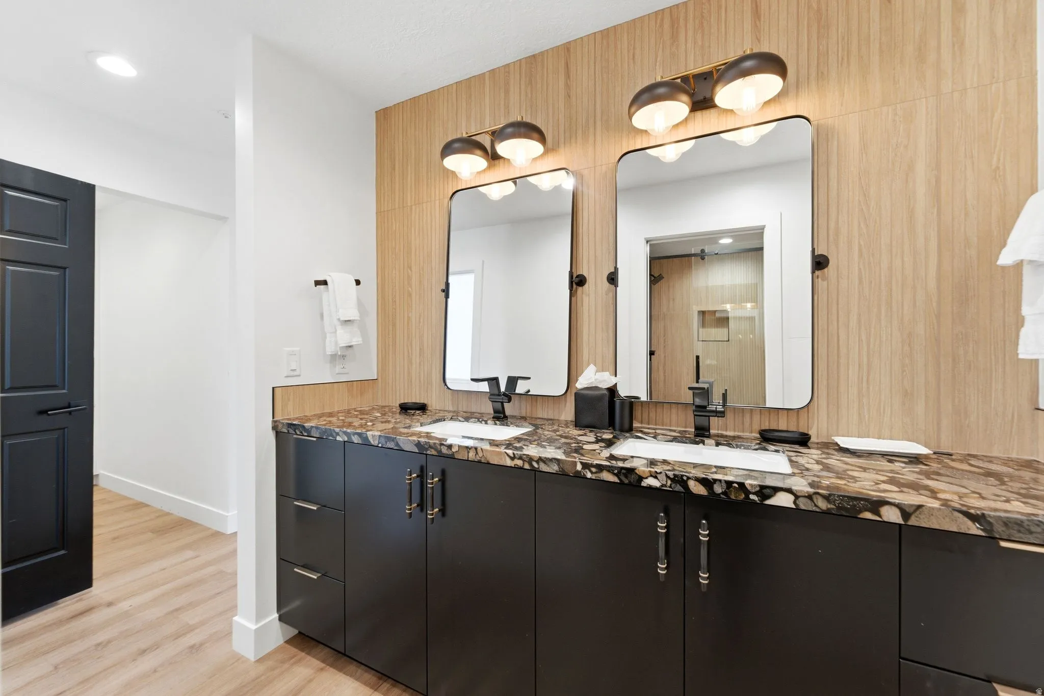 Dual vanity featuring dark cabinetry with decorative hardware, a patterned stone countertop, and two rectangular mirrors with integrated lighting