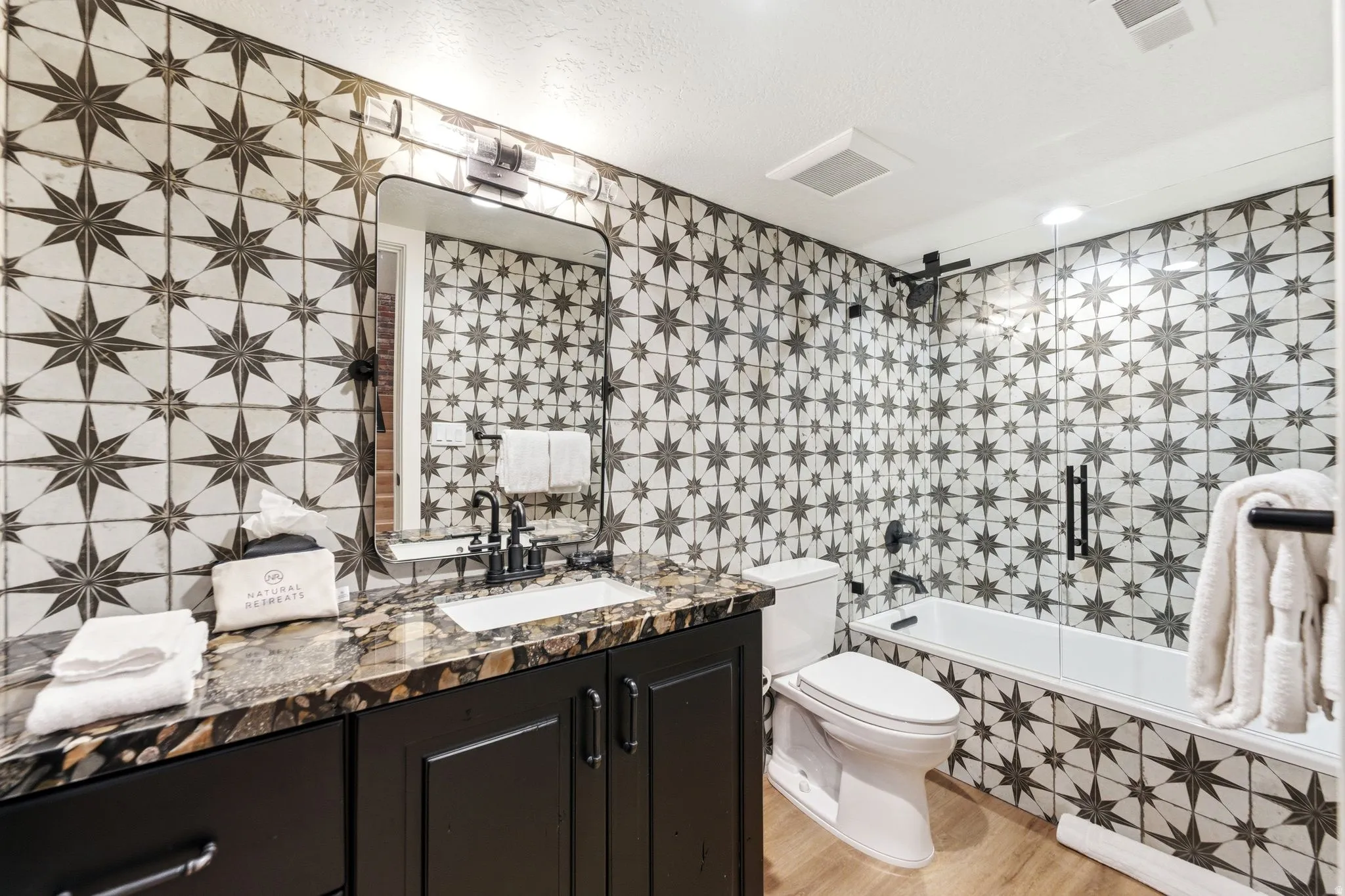 Bathroom featuring a patterned tile surround, dark wood vanity with a stone countertop, a rectangular undermount sink, and a framed mirror