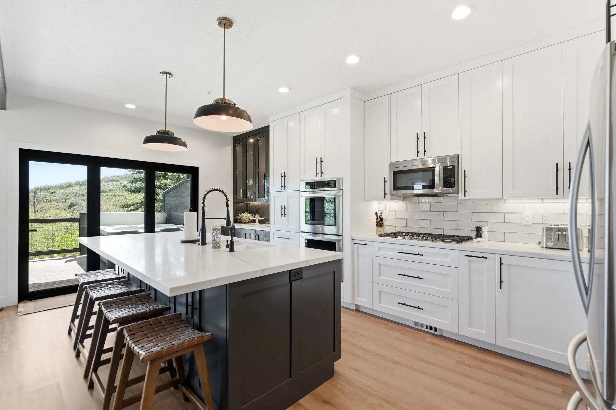 Gourmet kitchen featuring a substantial island with seating, stainless steel appliances, white subway tile backsplash, and wood-finish flooring