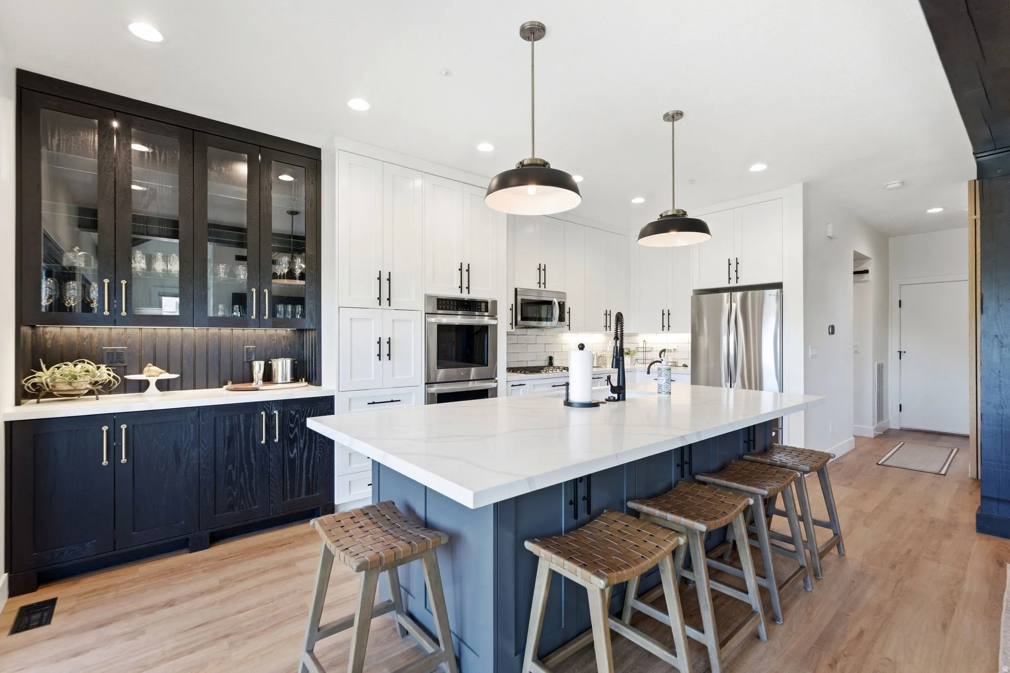 Kitchen featuring a large island with a light-colored countertop, pendant lighting, stainless steel appliances, and wood-finish flooring