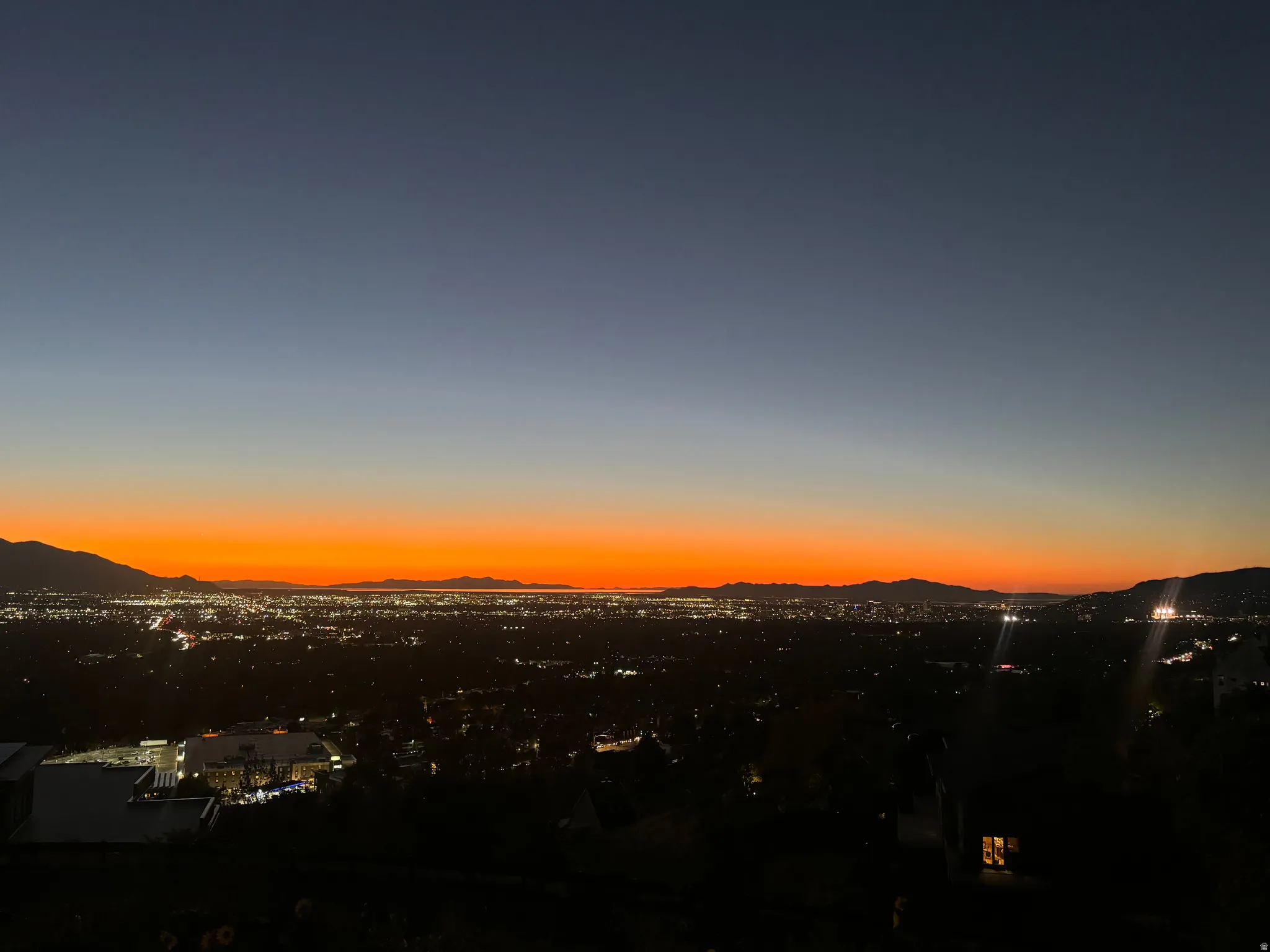 Expansive cityscape with distant mountains under a vibrant orange and blue twilight sky