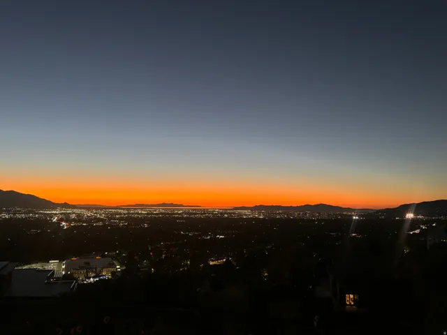 Expansive cityscape with distant mountains under a vibrant orange and blue twilight sky