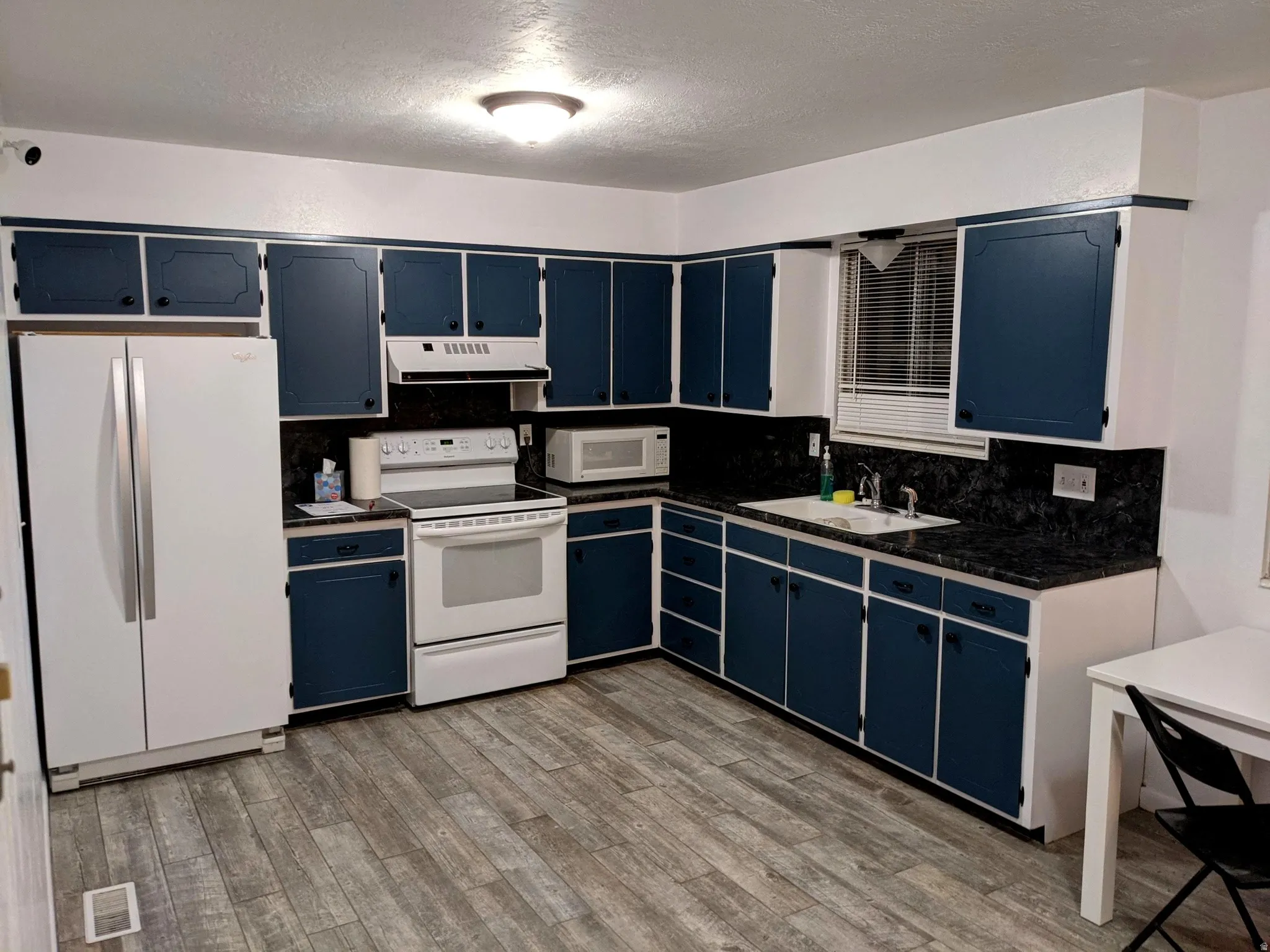 Kitchen with blue cabinetry, dark countertops, white appliances, backsplash,