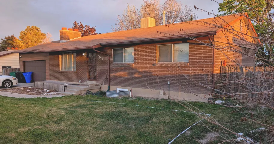 View of side of property featuring a chimney, brick siding, an attached garage, and a lawn