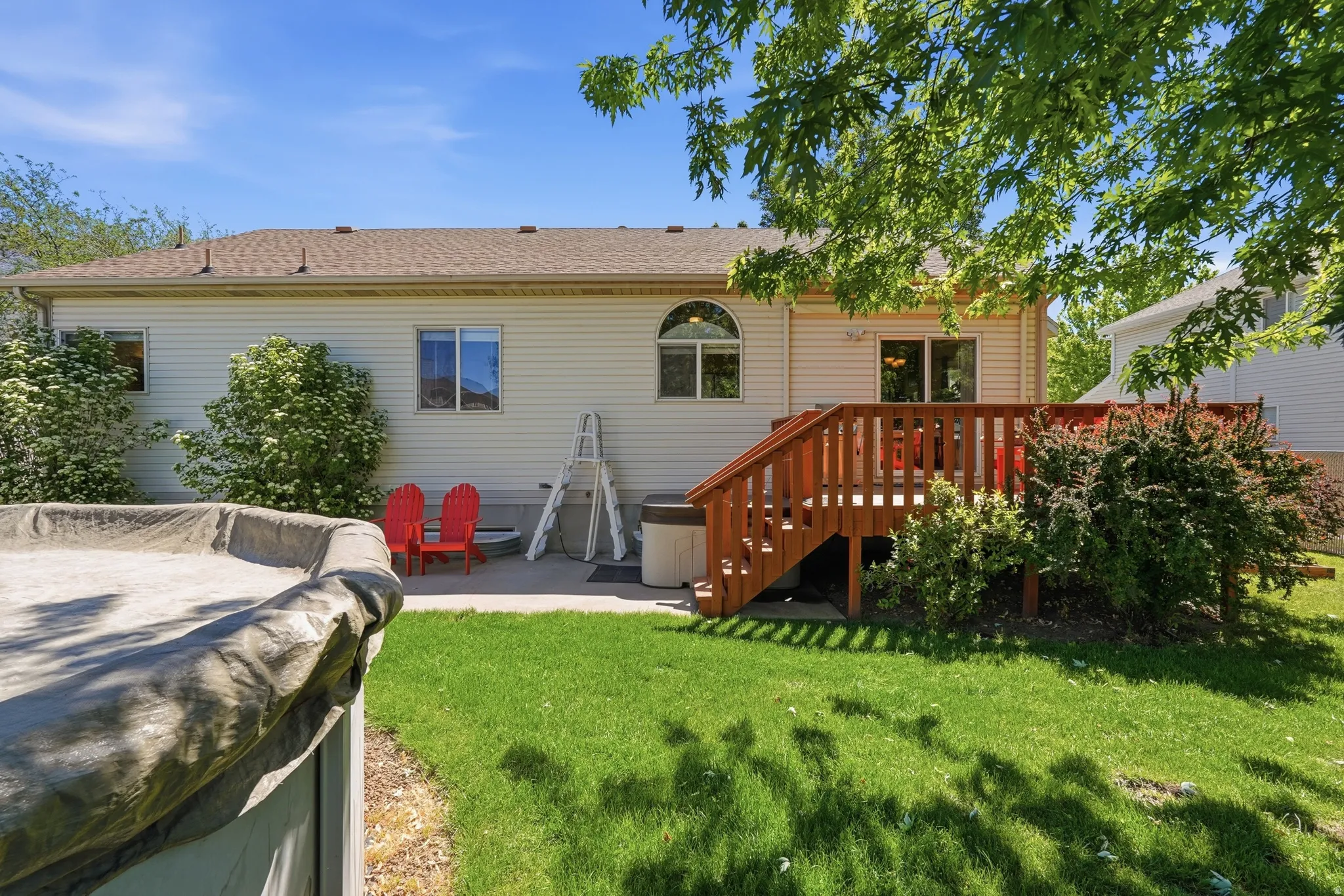 Rear exterior featuring a wood-finish deck with railings, a manicured lawn, and mature trees providing natural shade