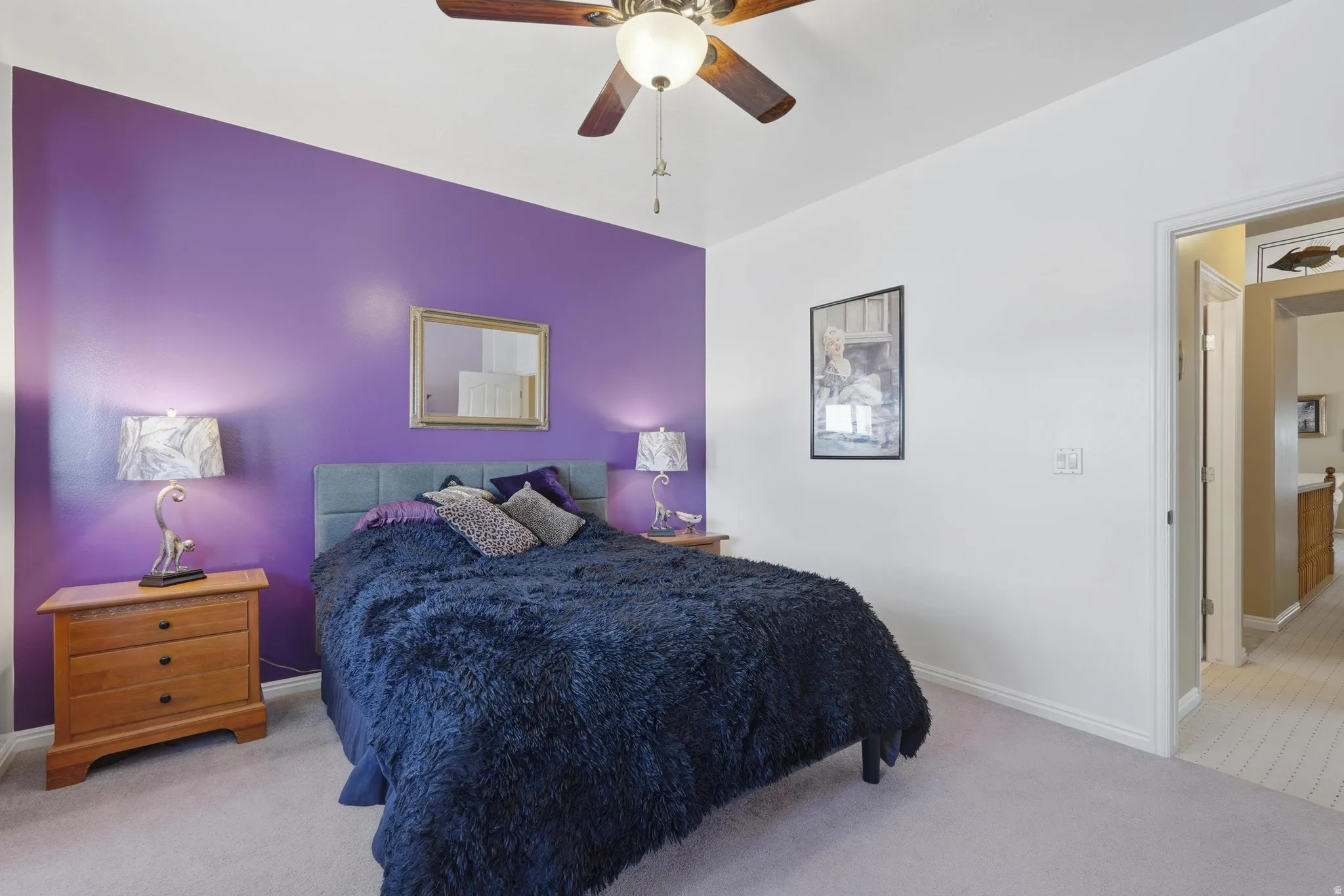 Bedroom featuring a purple accent wall, light gray carpeting, and a ceiling fan with integrated lighting