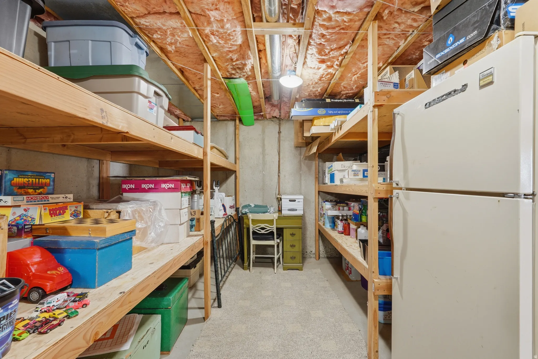 Basement storage area featuring extensive built-in wooden shelving and extra fridge