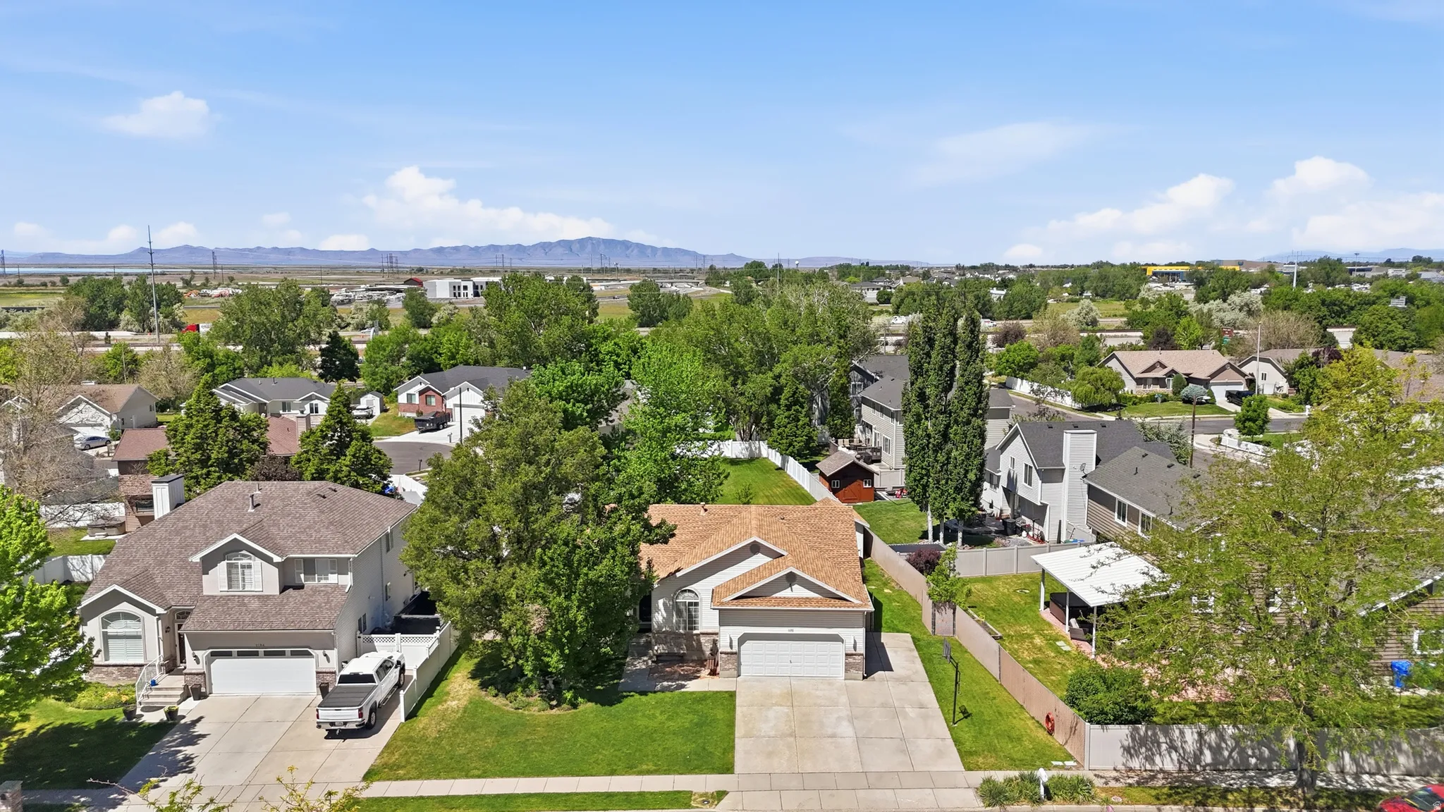 Suburban residence featuring a two-car garage, mature front yard trees, and a paved driveway