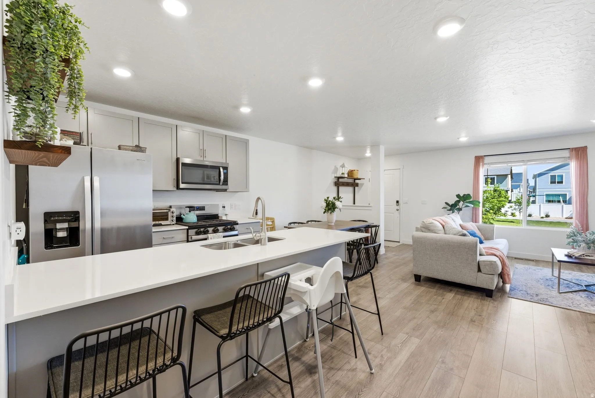Open-concept living space featuring a kitchen island with seating, stainless steel appliances, light gray cabinetry, and wood-finish flooring