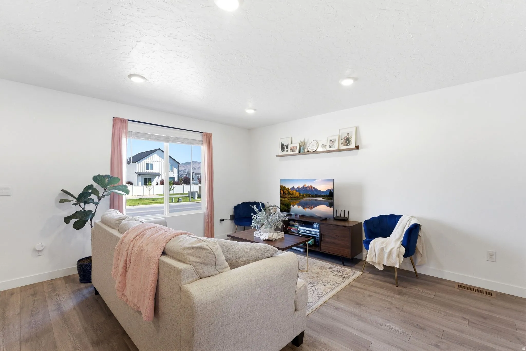 Bright living space featuring recessed lighting, wood-finish flooring, a large window, a wall-mounted display shelf, and a dark wood media console