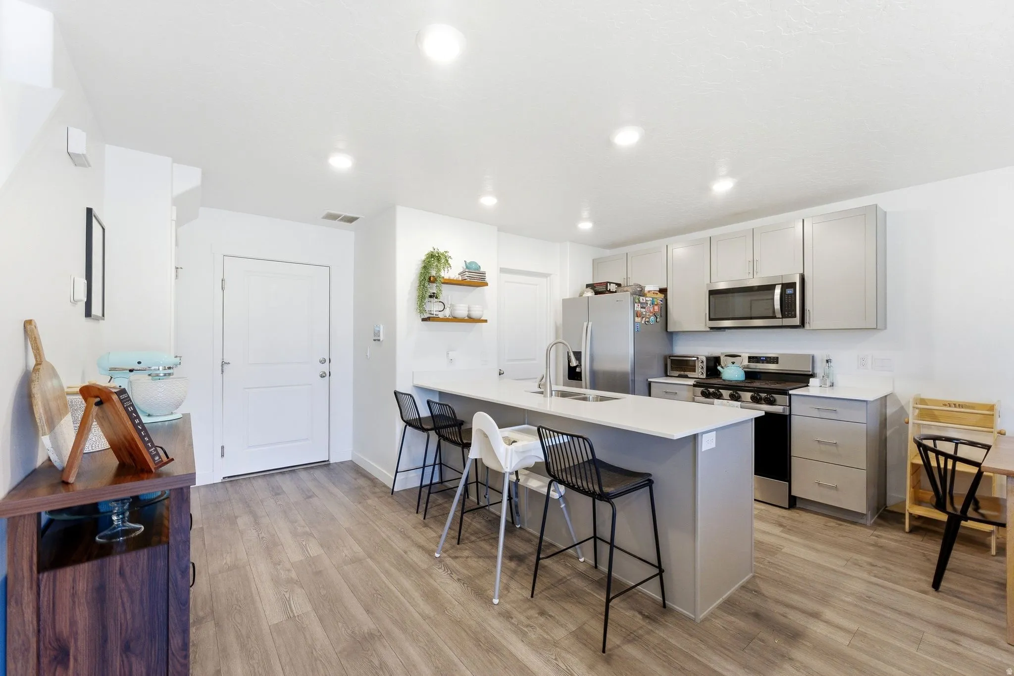Modern kitchen featuring light gray cabinetry, stainless steel appliances, a white solid surface countertop, an island with seating, and wood-finish flooring
