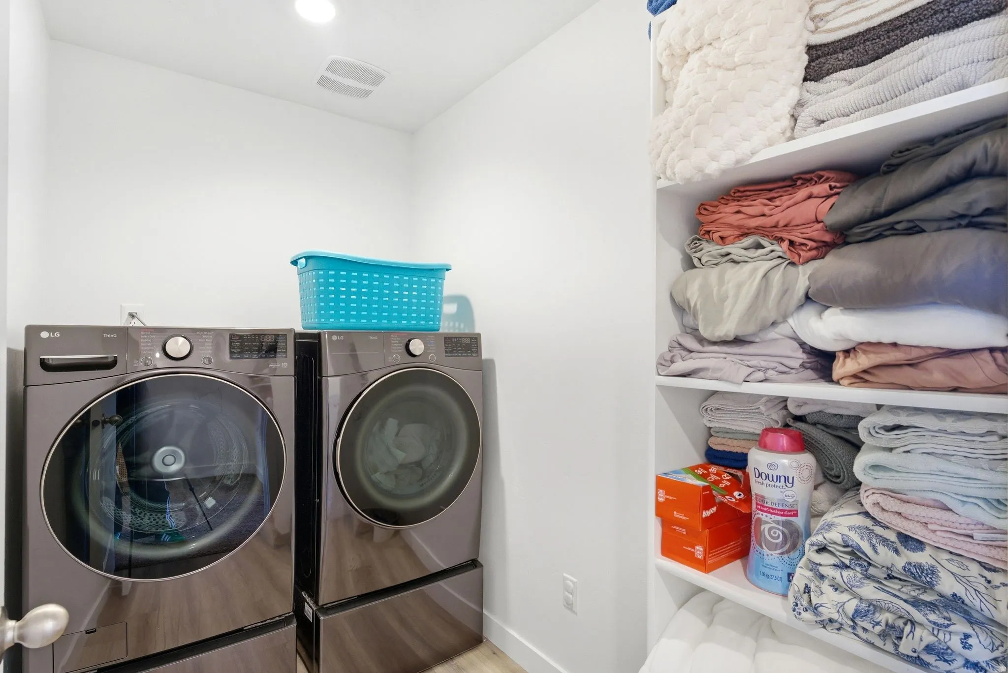 Dedicated laundry area featuring modern front-loading appliances on pedestals, overhead recessed lighting, and light wood-finish flooring
