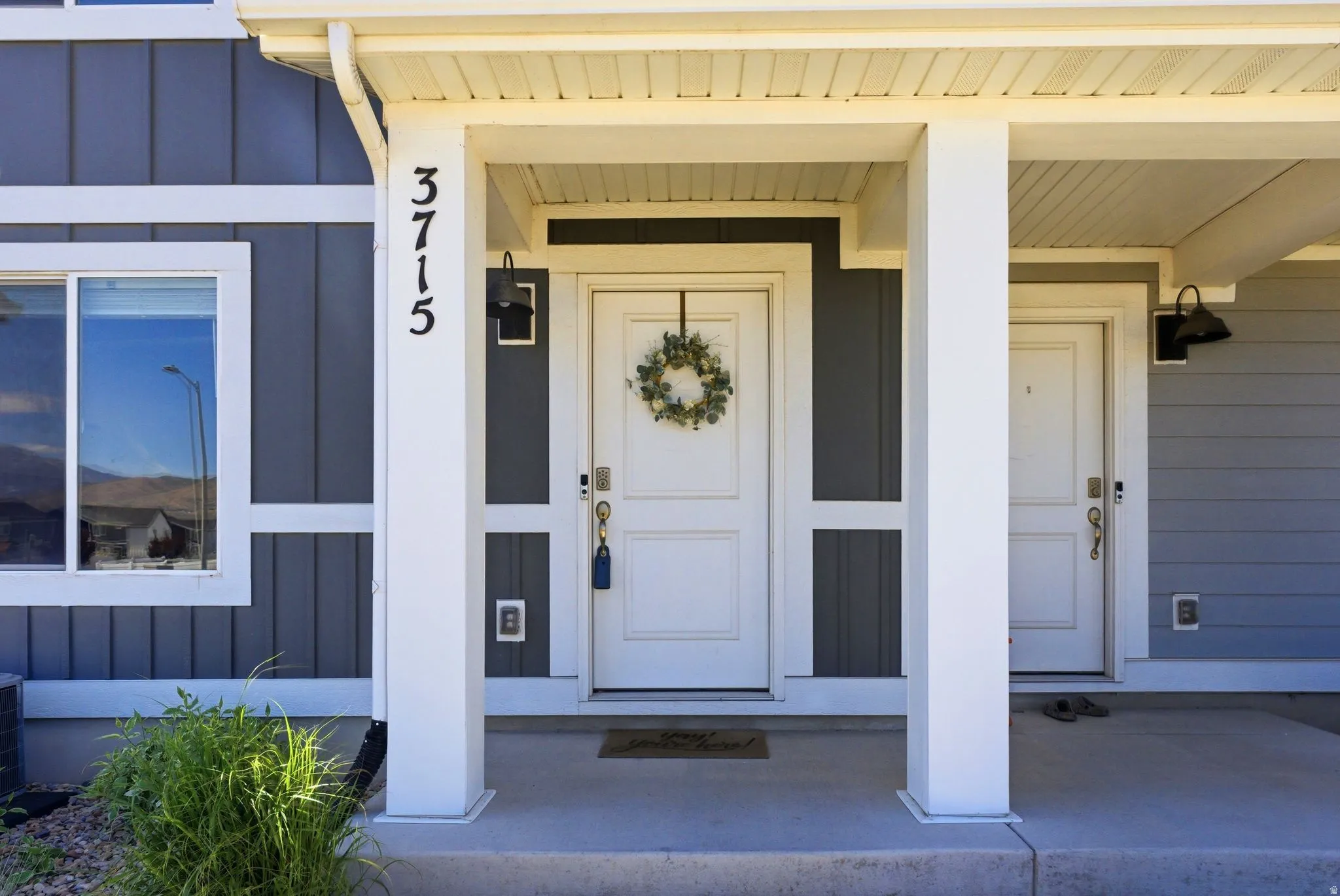 Covered entry with two white doors, contemporary exterior lighting, and a grey vertical siding facade