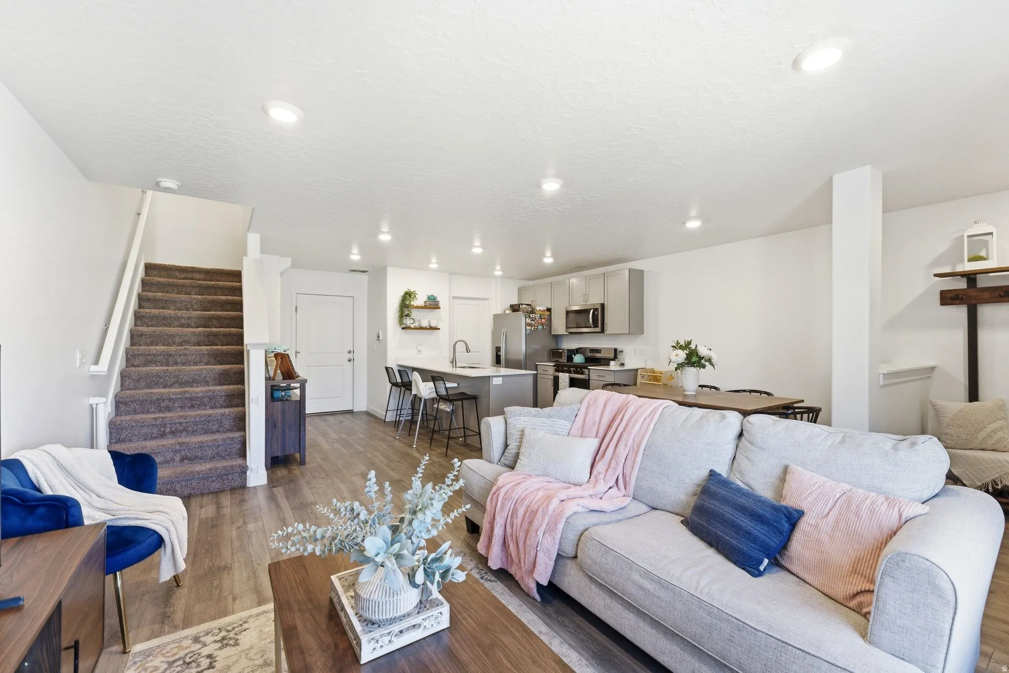 Open-concept living space featuring wood-finish flooring, recessed lighting, and a modern kitchen with grey cabinetry and stainless steel appliances