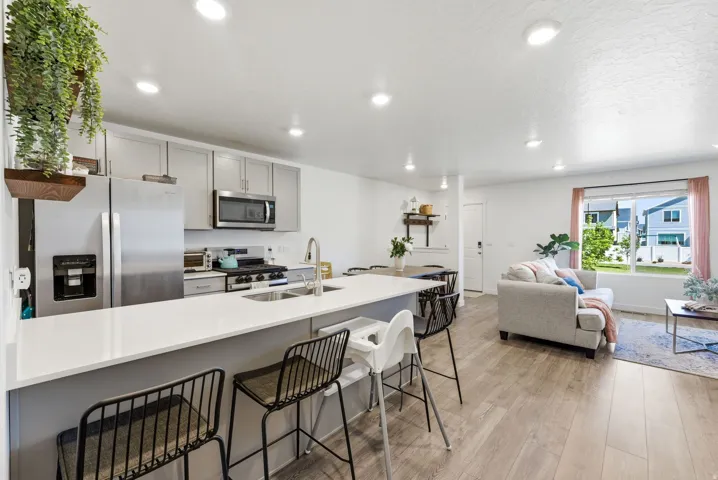 Open-concept living space featuring a kitchen island with seating, stainless steel appliances, light gray cabinetry, and wood-finish flooring