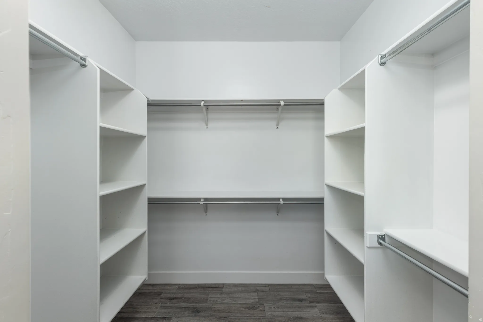 Walk-in closet featuring white built-in shelving, multiple hanging rods, and wood-finish flooring