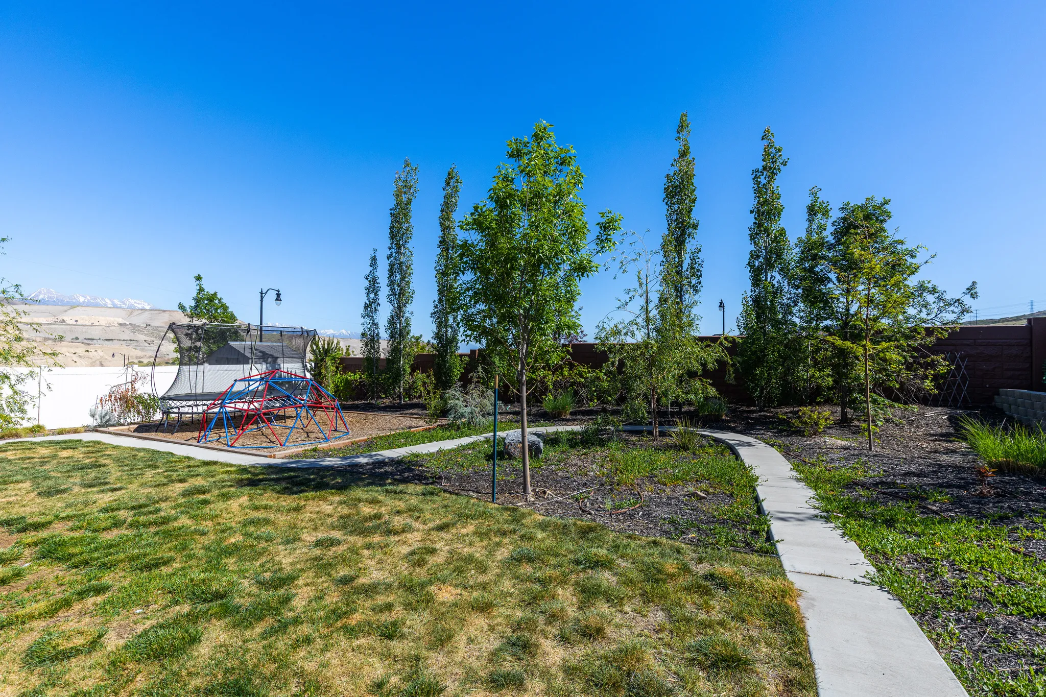 Expansive backyard featuring a concrete pathway, mature trees, and a terraced landscape
