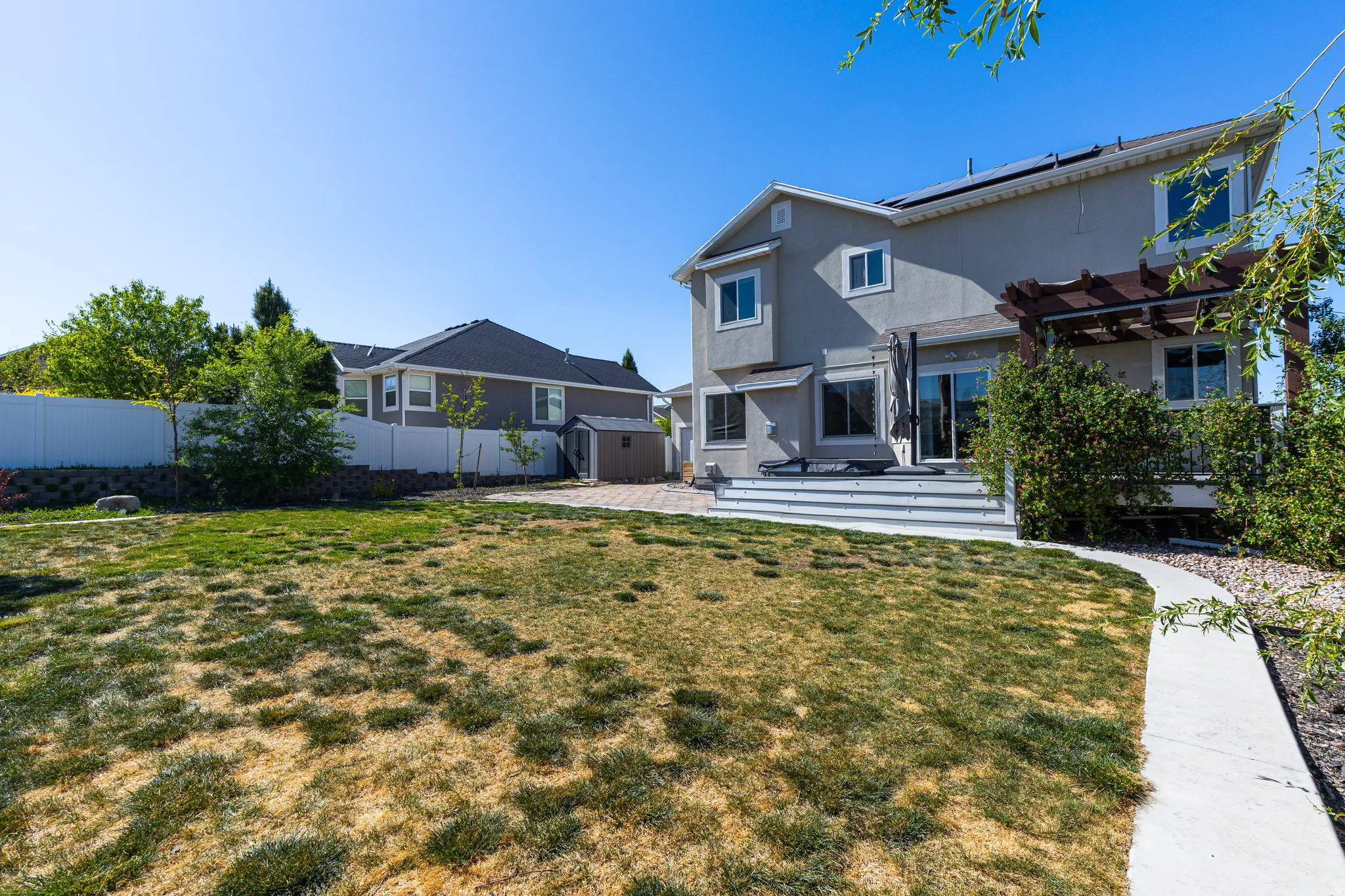 Expansive backyard featuring a concrete pathway, a multi-level deck with a pergola, and a storage shed