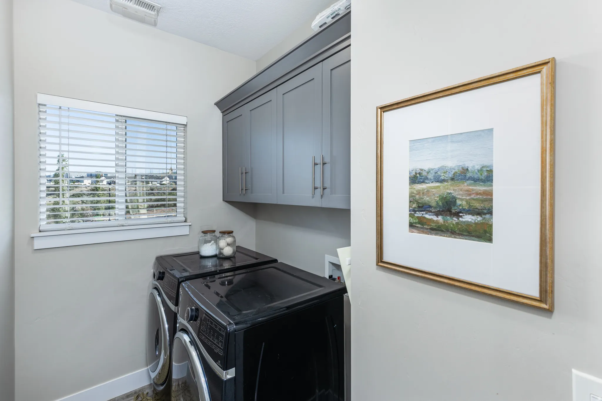 Laundry area featuring upper cabinetry with brushed nickel hardware, light neutral wall paint, and a window with blinds