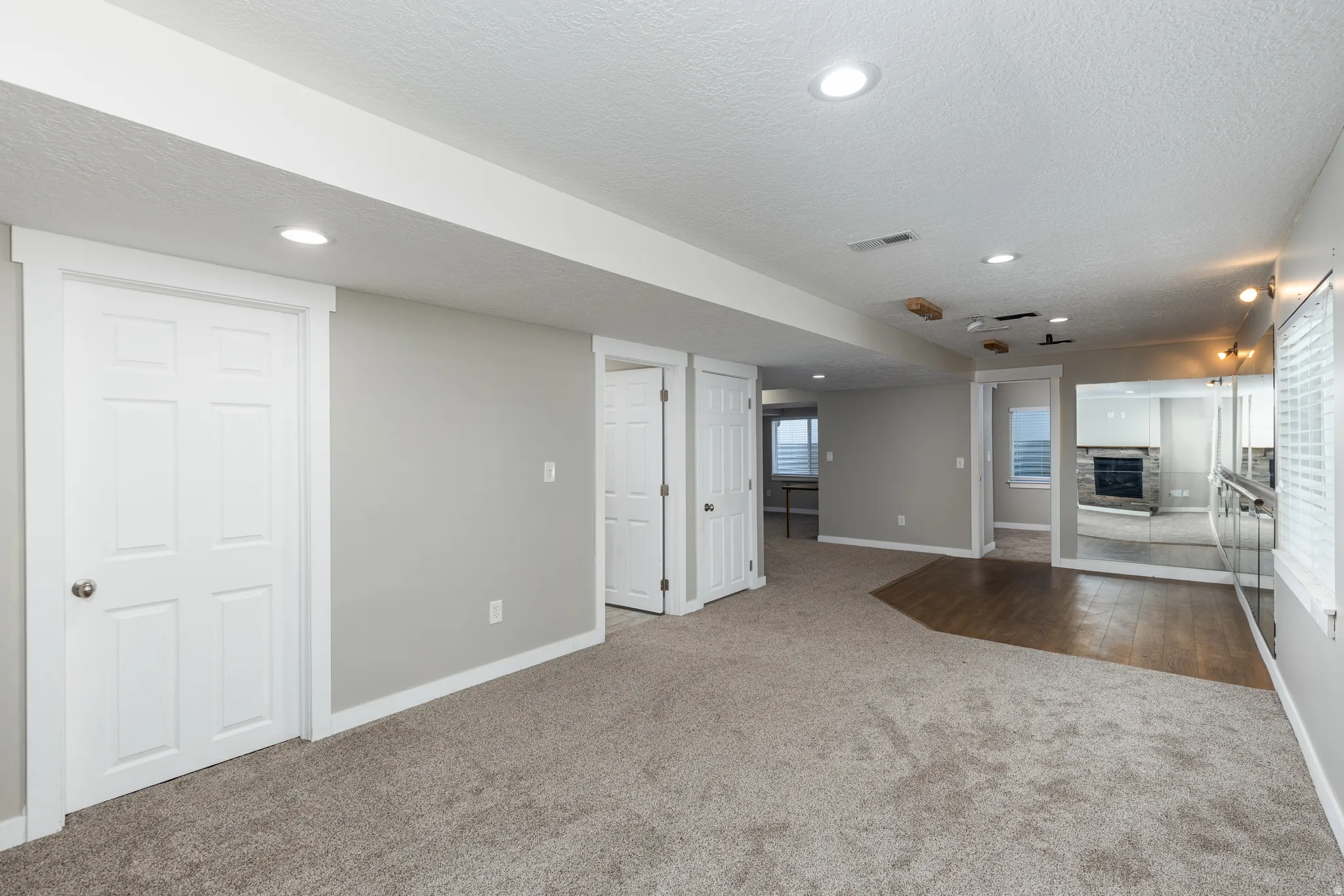 Spacious room featuring neutral carpeting, a wood-finish flooring section, recessed lighting, and a mirrored wall with a ballet barre