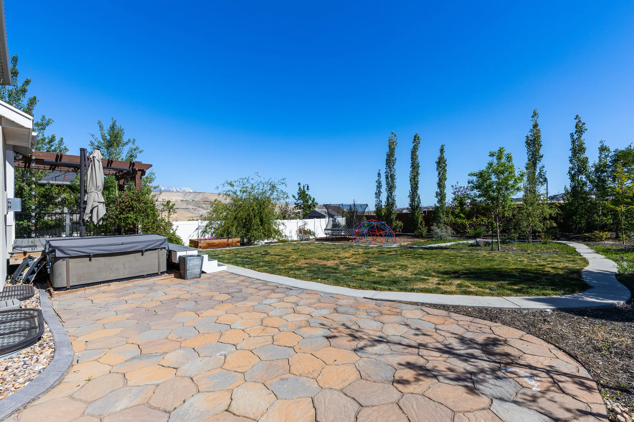 Expansive backyard featuring a multi-toned paver patio, a built-in hot tub, and a pergola structure