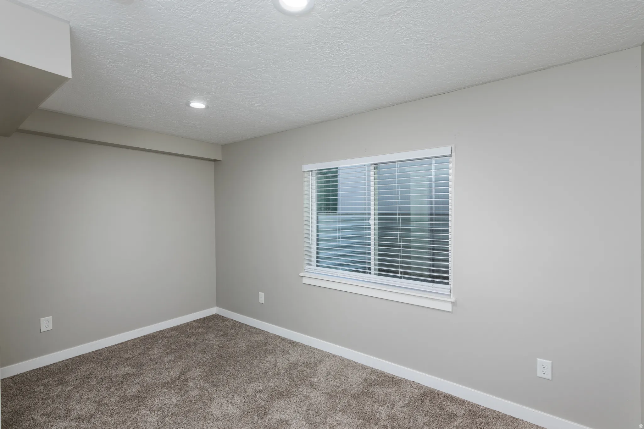 Carpeted room with a horizontal sliding window featuring white blinds, recessed lighting, and light gray wall paint with white trim