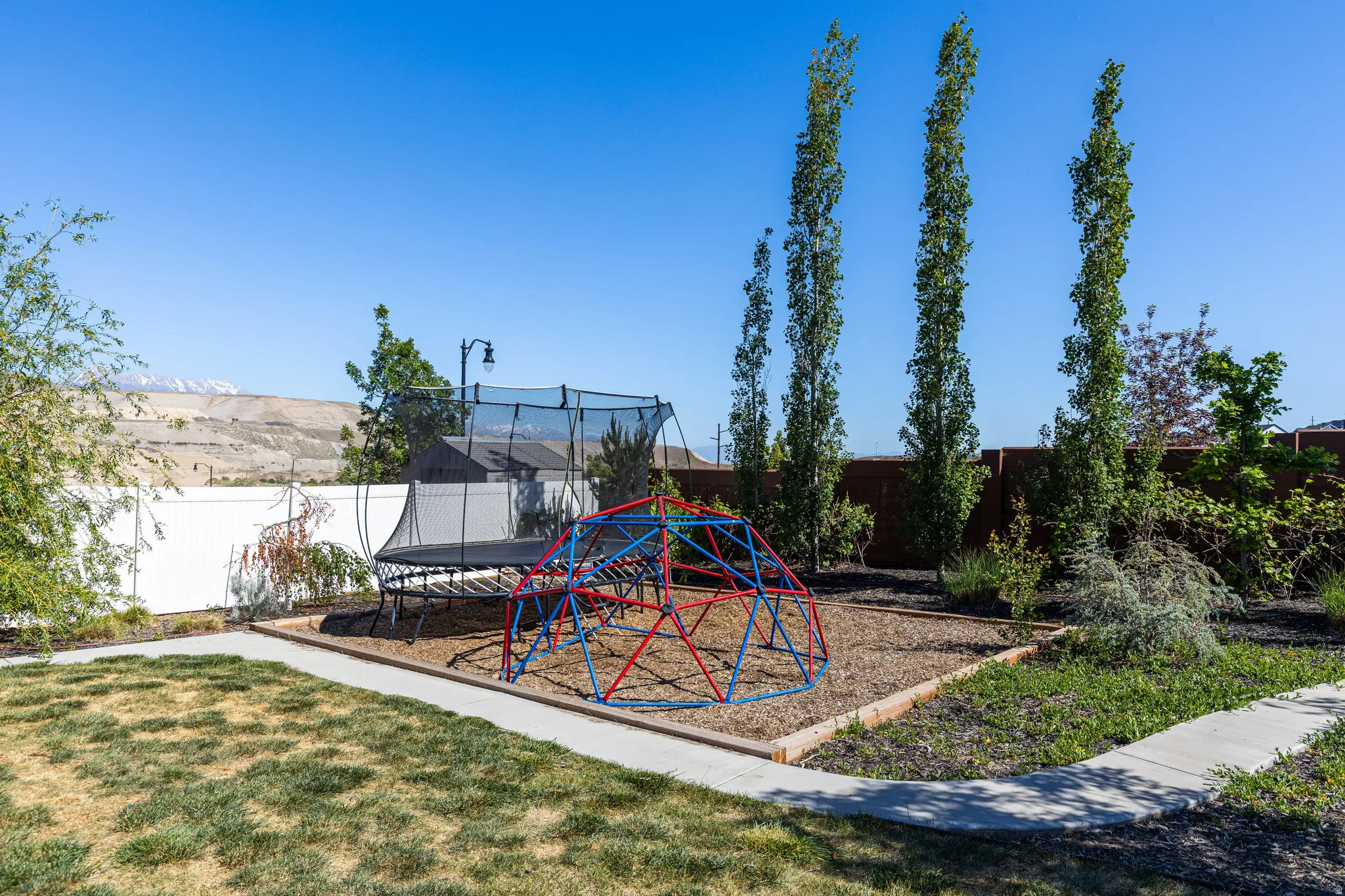 Backyard featuring a concrete pathway, a mulched area, and mature trees
