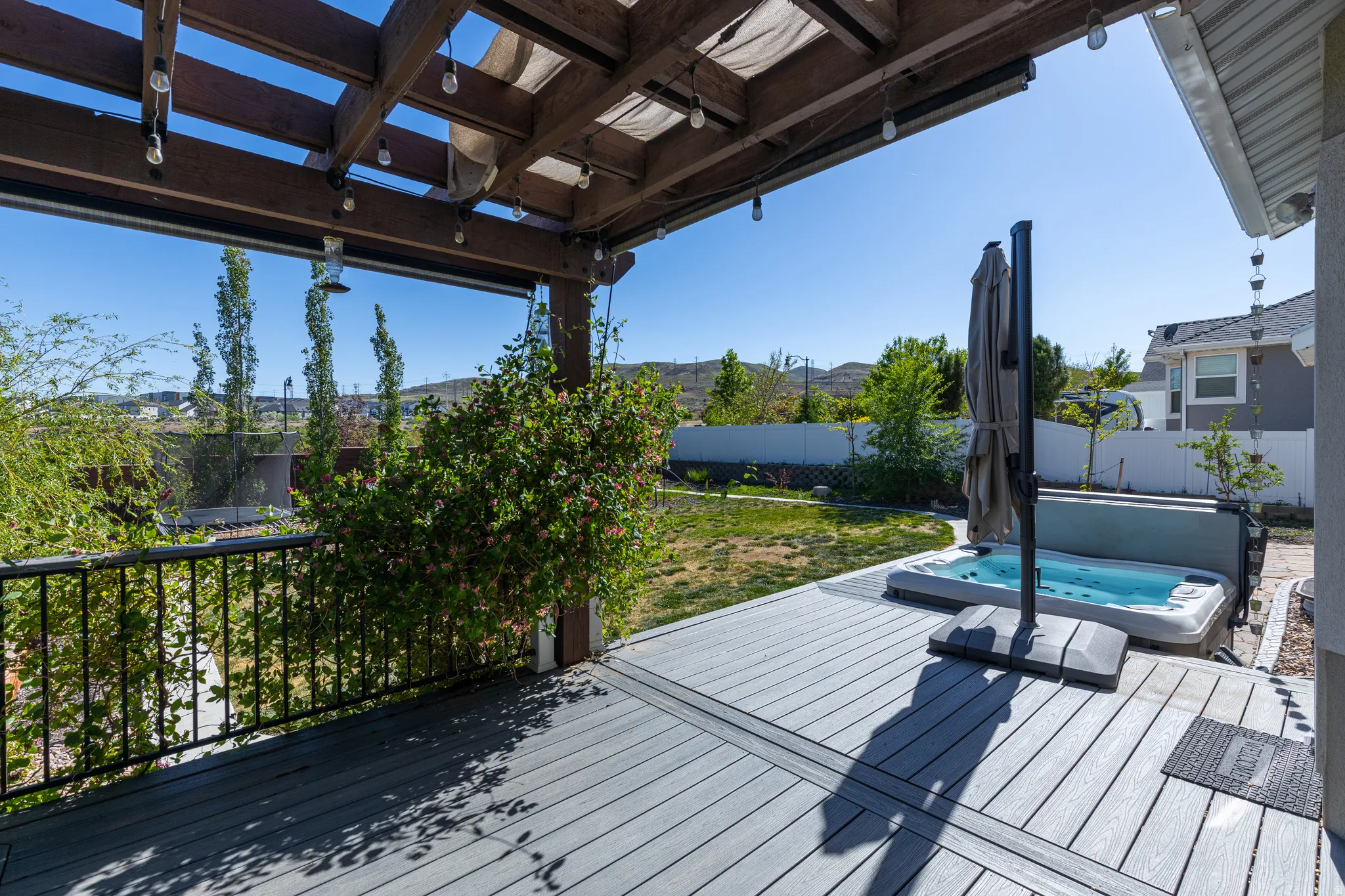 Outdoor deck featuring a hot tub, wood pergola with string lighting, and black metal railing